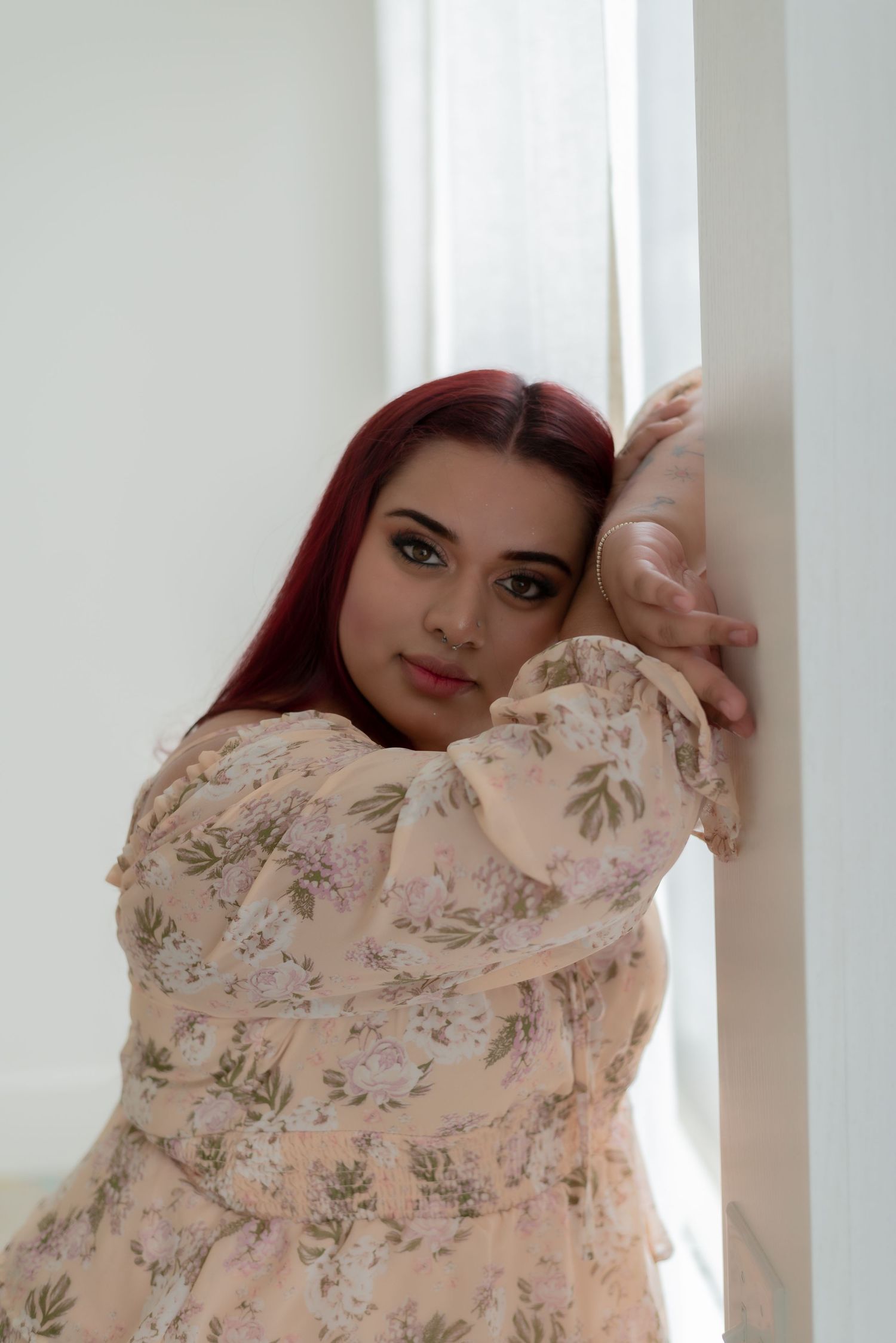 Dreamy portrait against white curtains showing someone in a floral peach-colored dress.
