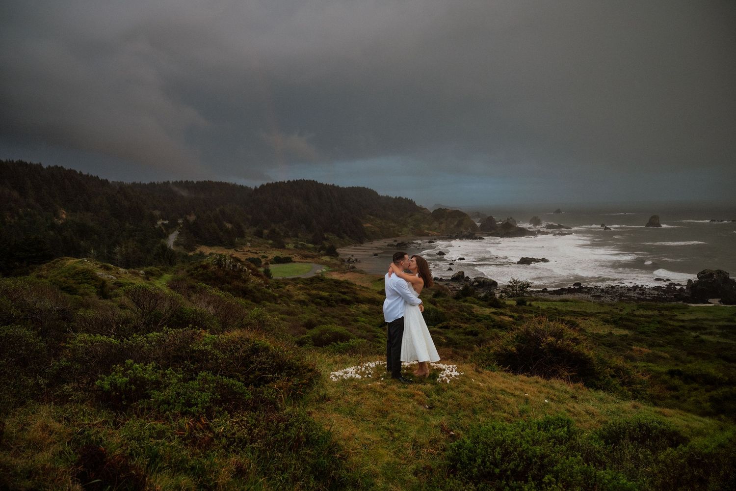 A couple embraces on a dramatic coastal cliff overlooking the ocean on their wedding day.