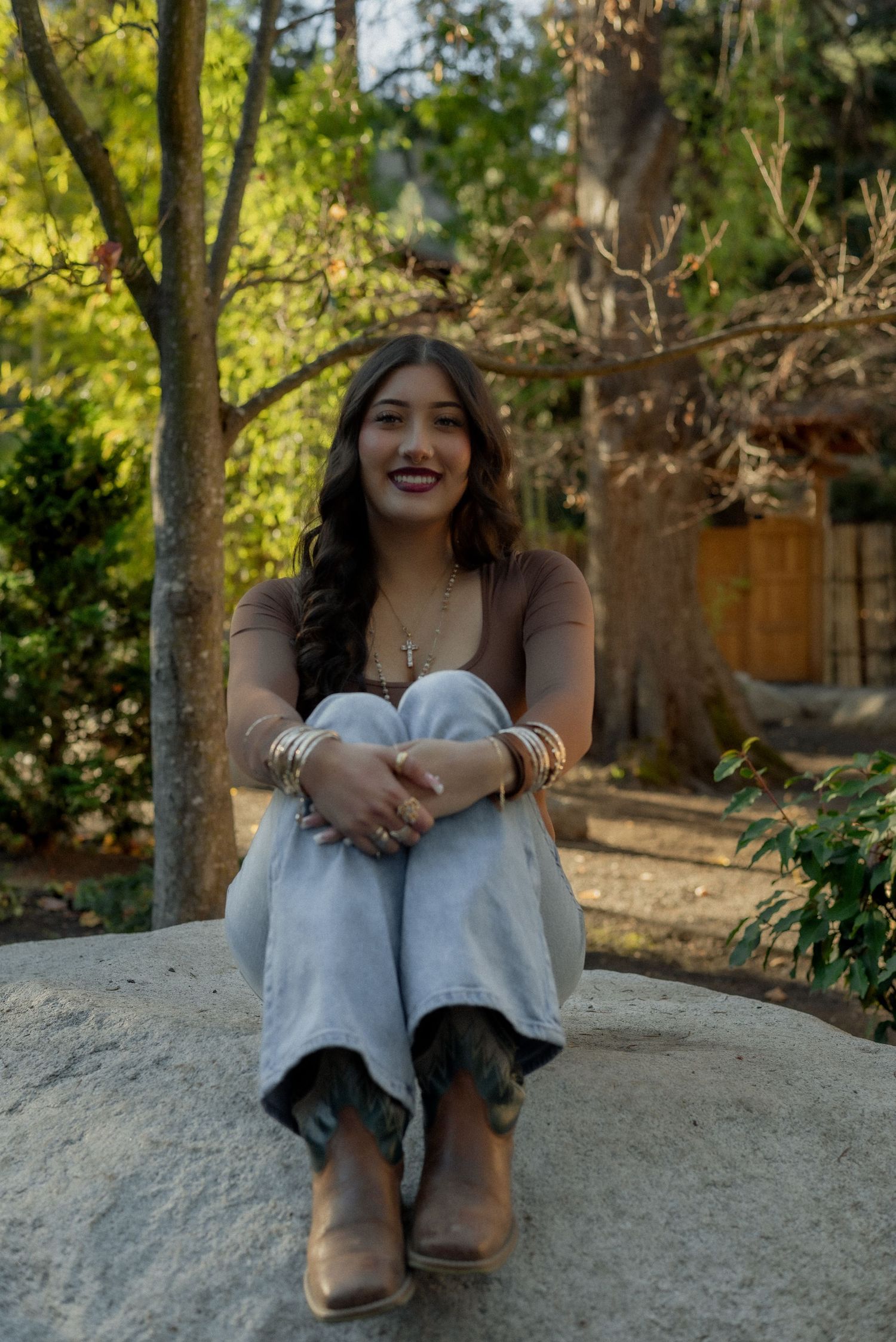 Outdoor portrait session on a large rock with casual denim and brown top in natural lighting.