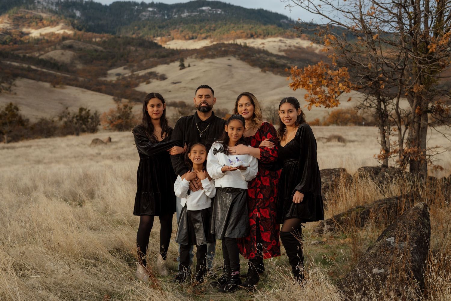 A group poses together on a hillside during autumn with mountains and dry grass in the background.