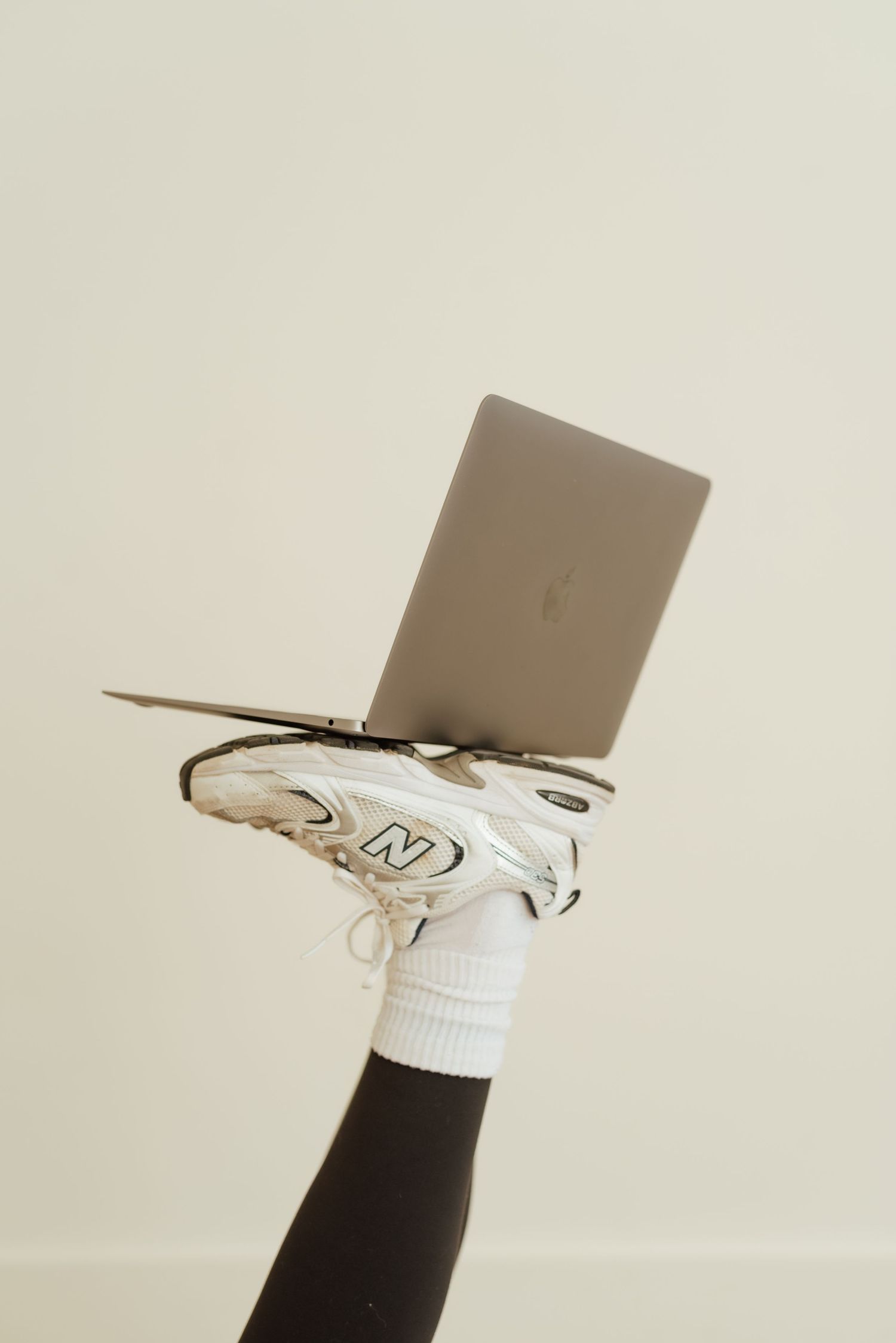 Close-up of white sneakers with laptop balanced precariously on top against light background.