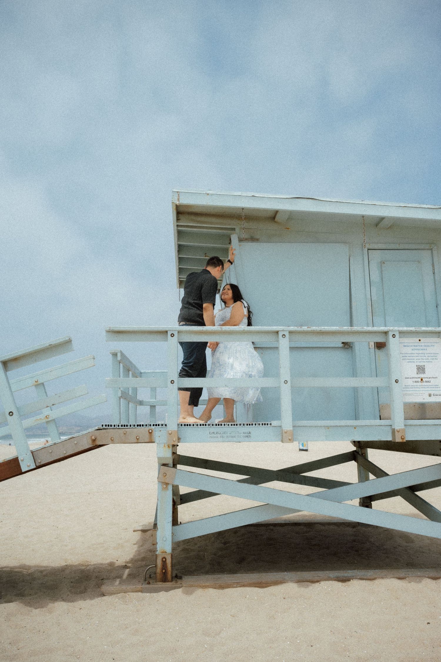 A couple shares a moment on a white lifeguard tower at the beach.