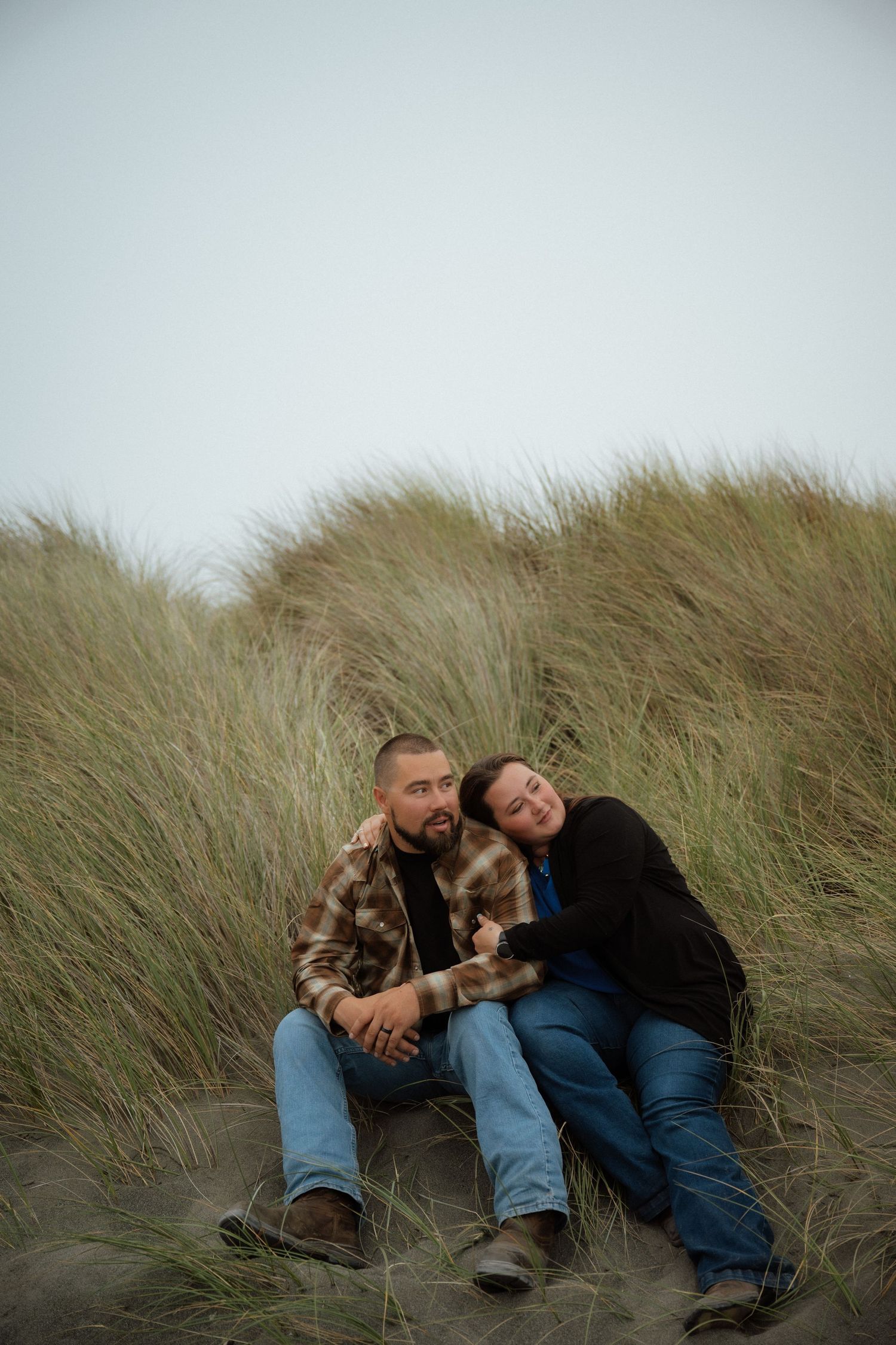 A couple relaxes together in beach grass during an intimate photoshoot.