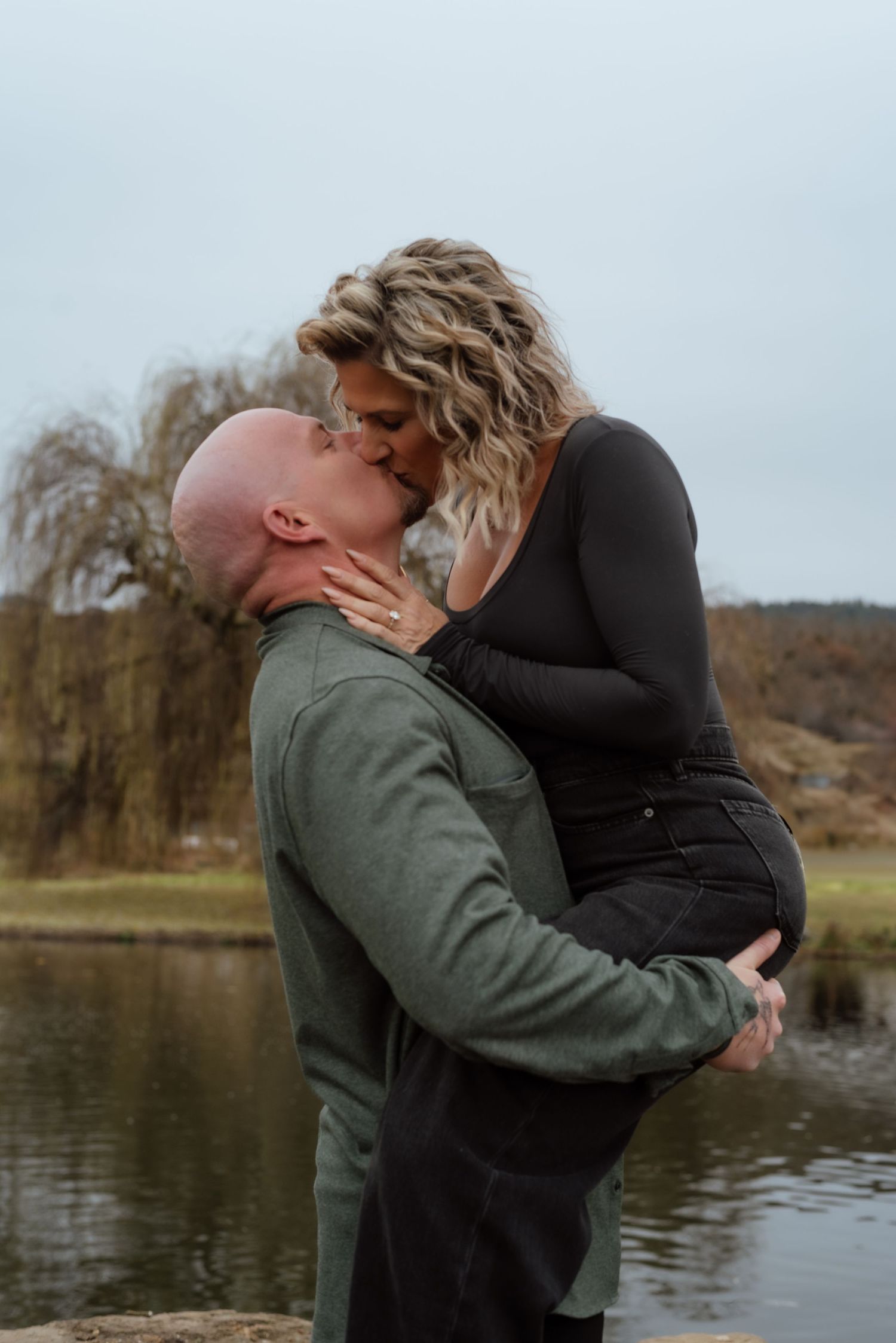 Couple sharing a passionate kiss while embracing near a tranquil pond.