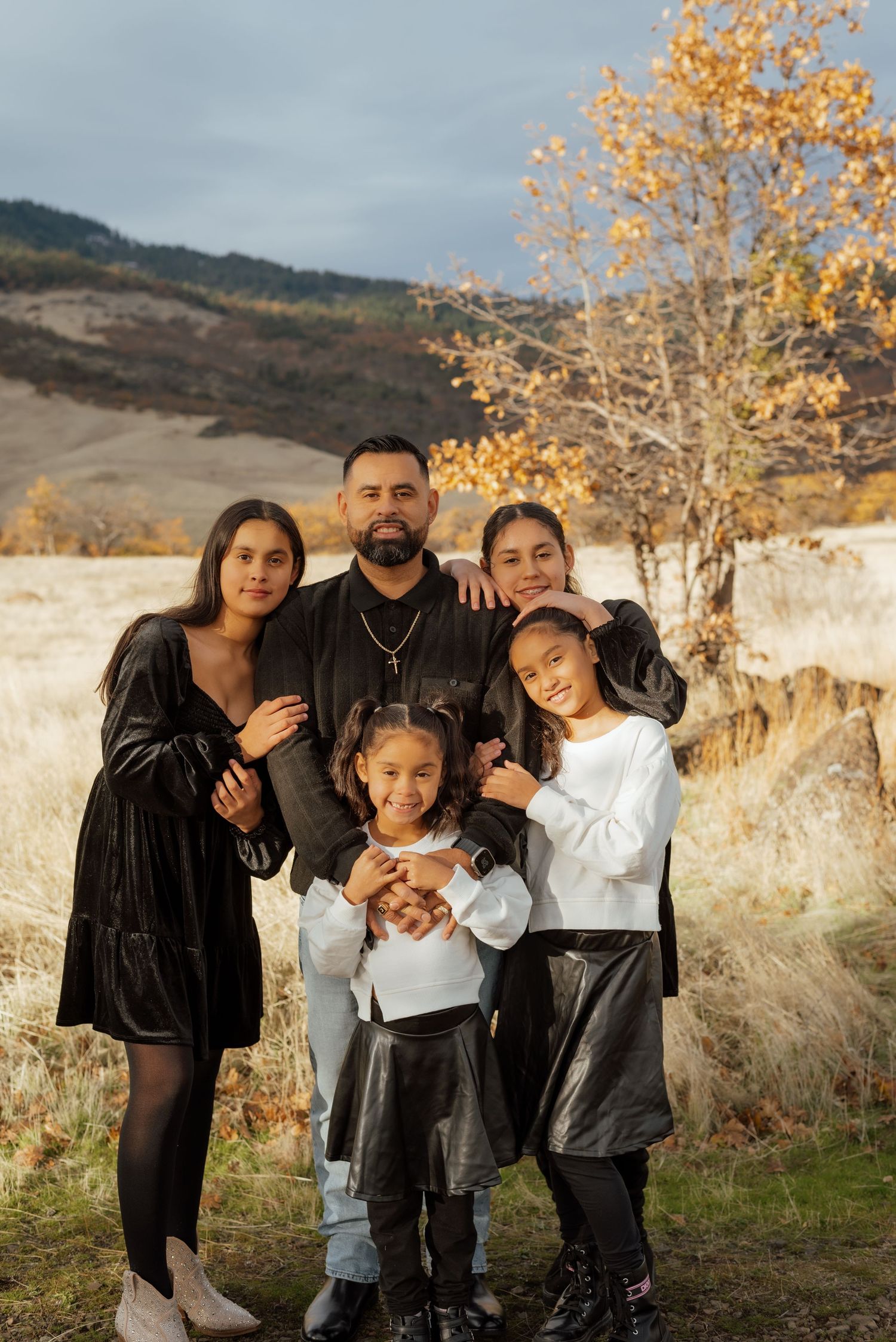 Family portrait in coordinated black and white outfits against an autumn mountain backdrop.