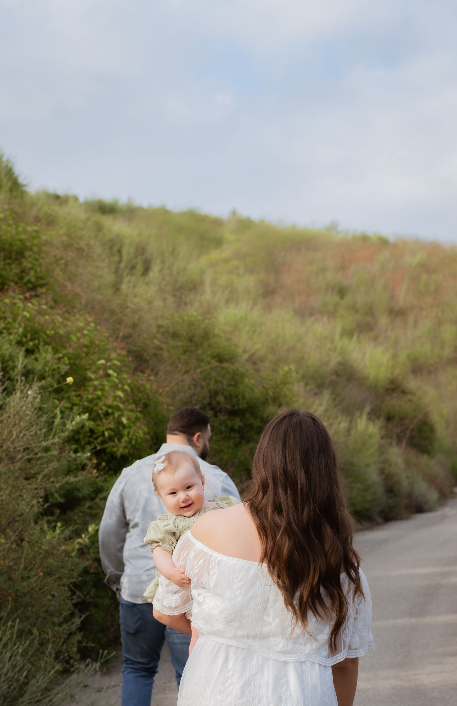 A tender family moment captured on a winding path with green hills in the background.