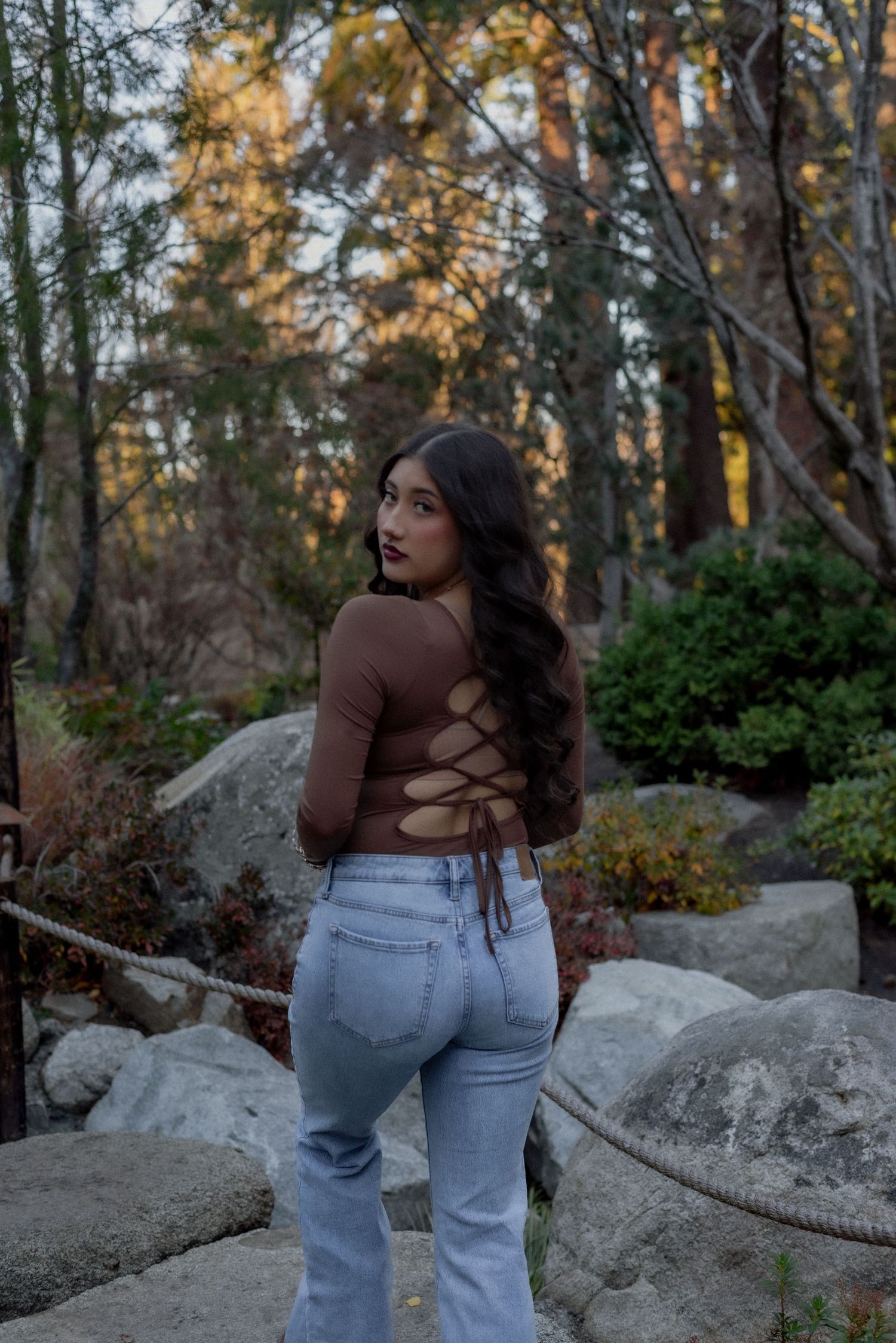 Fashion photography in nature featuring light denim and brown top against rocky outdoor backdrop.