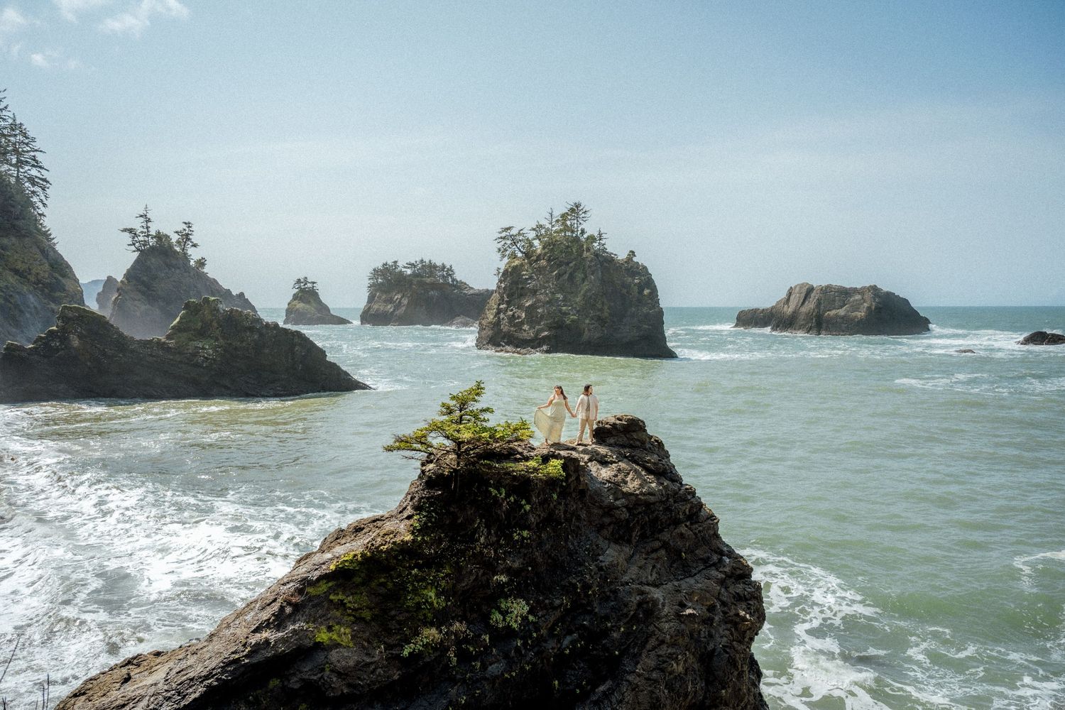 Dramatic coastal landscape with rocky outcrops and crashing waves against a blue sky.