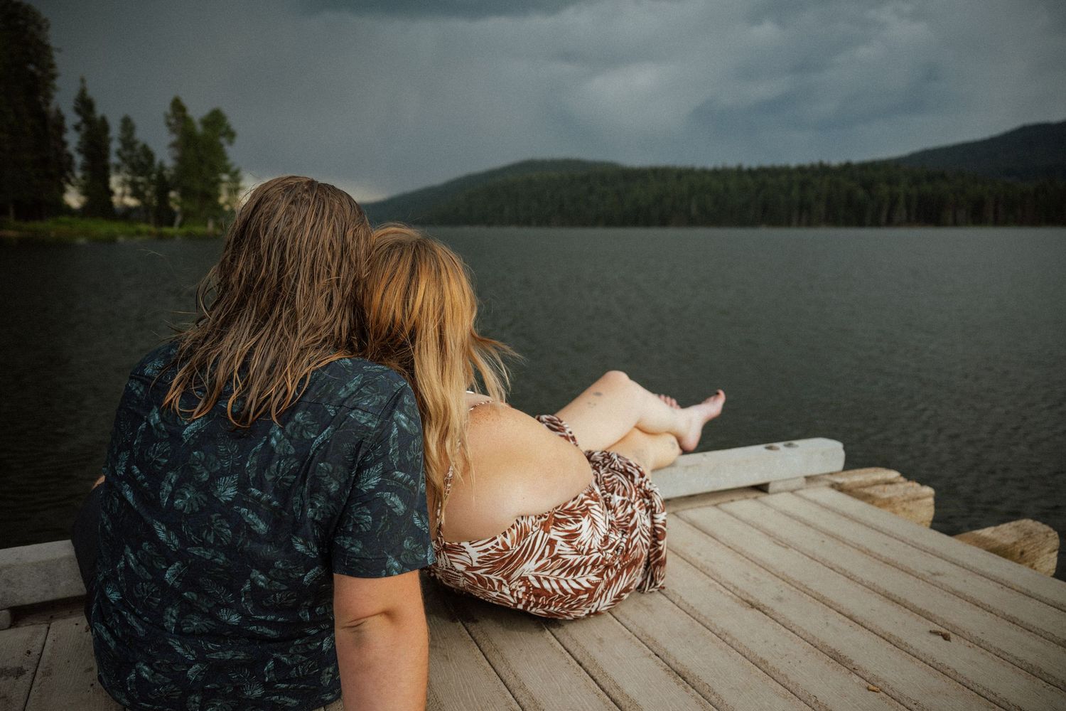 Couple relaxing together on a wooden dock overlooking a mountain lake.