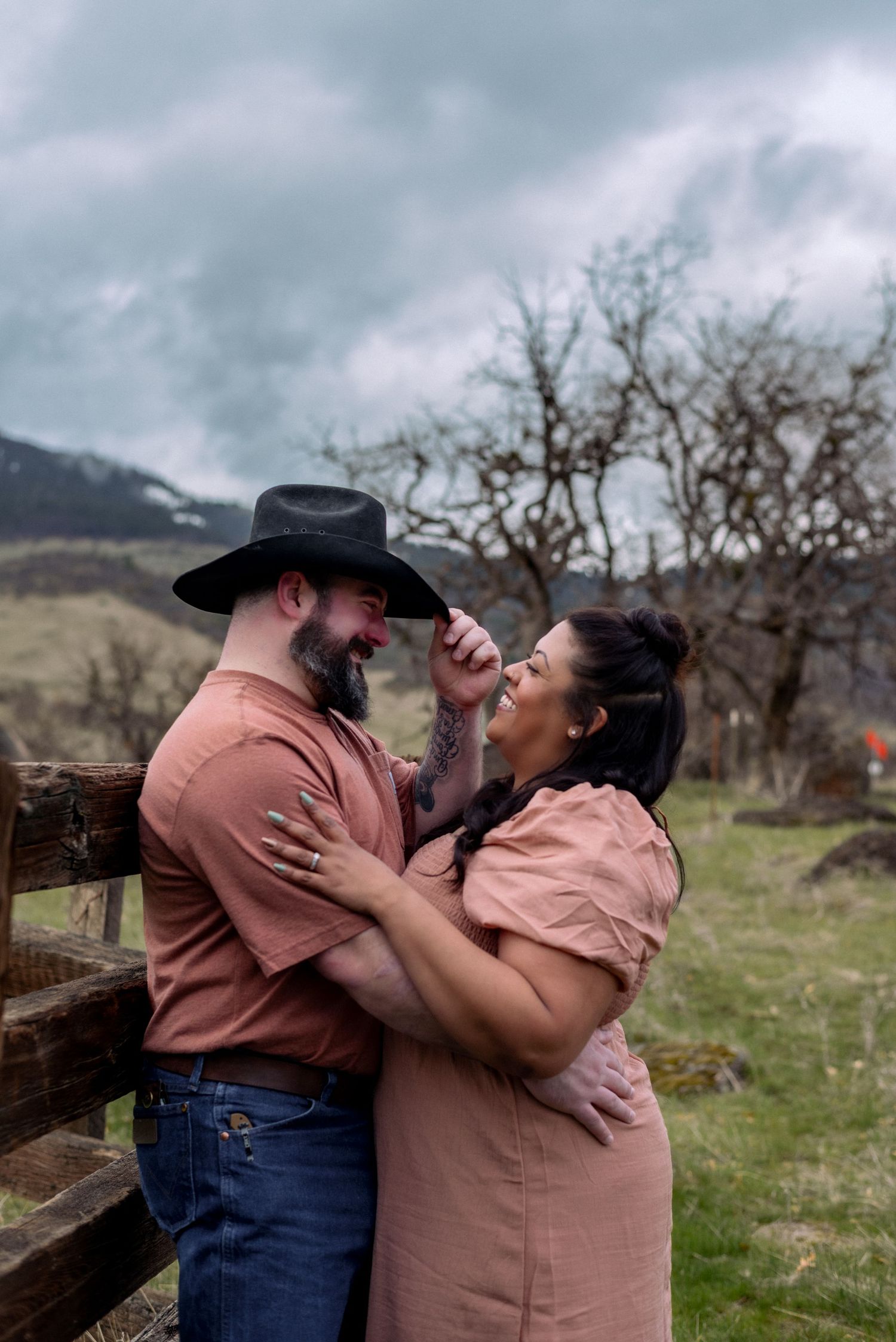 A couple shares intimate moments by a rustic fence with mountains in the distance.