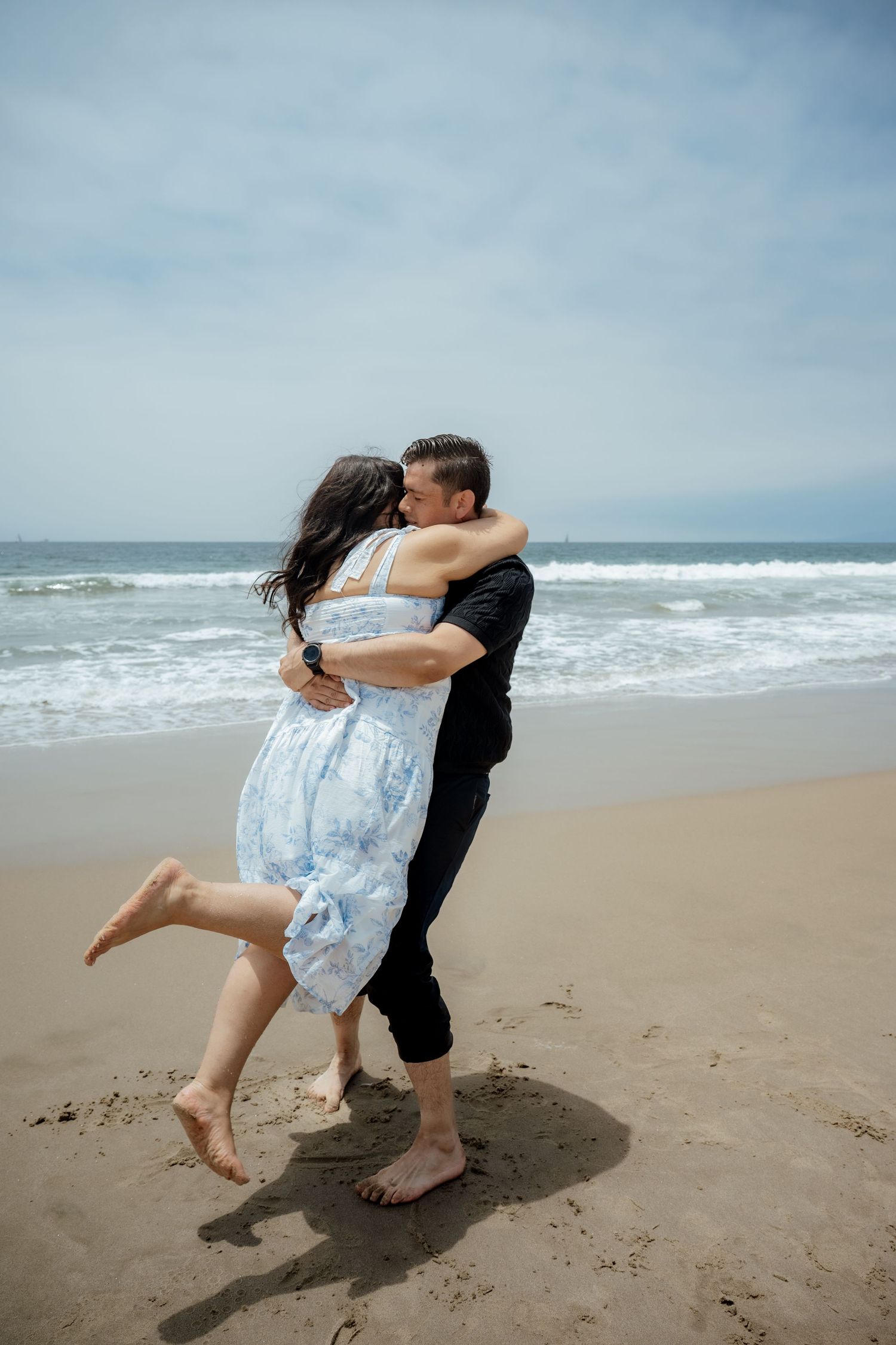 A couple dances playfully on the beach in front of ocean waves.