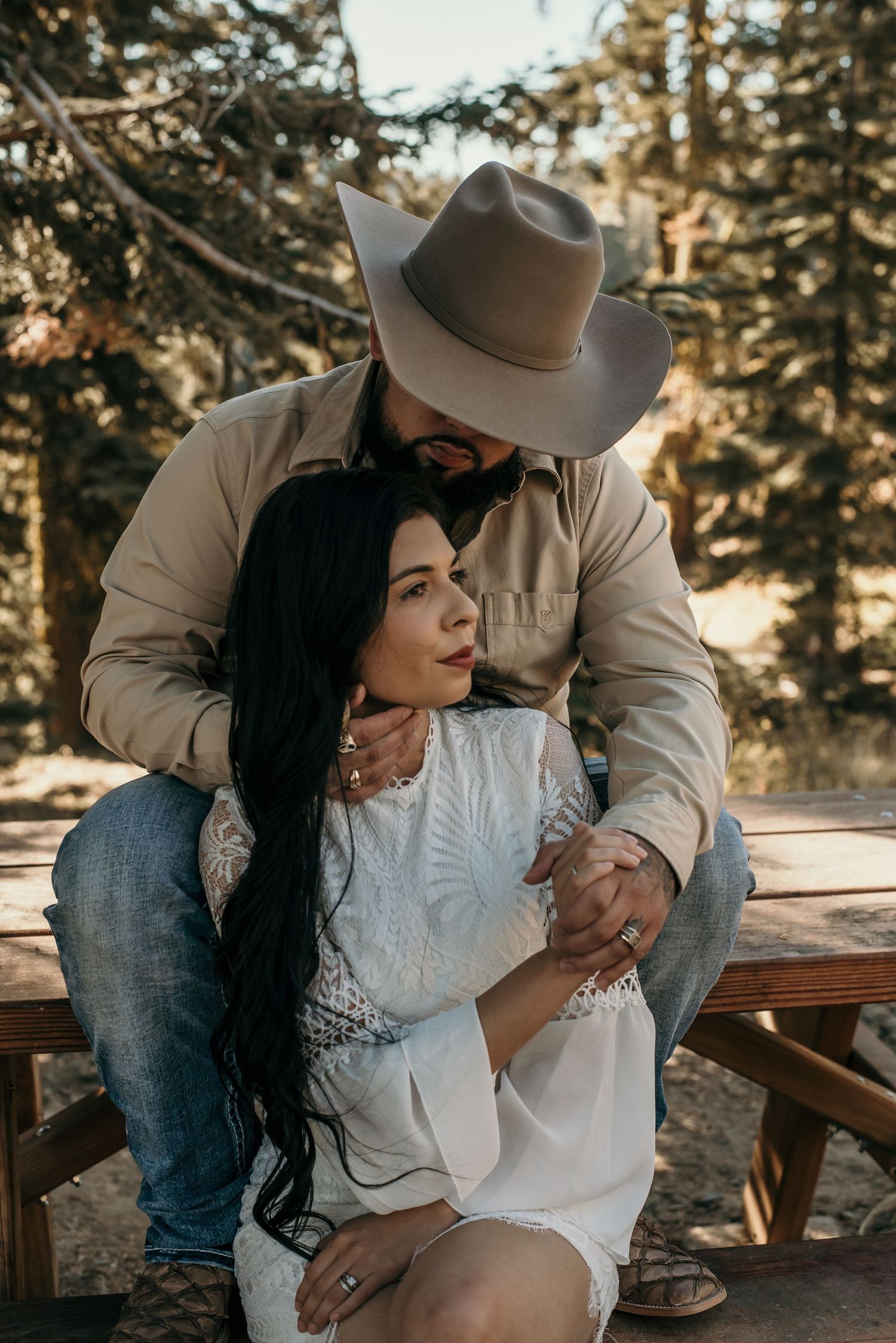 A tender moment shared between a couple on a wooden bench in a mountain setting.