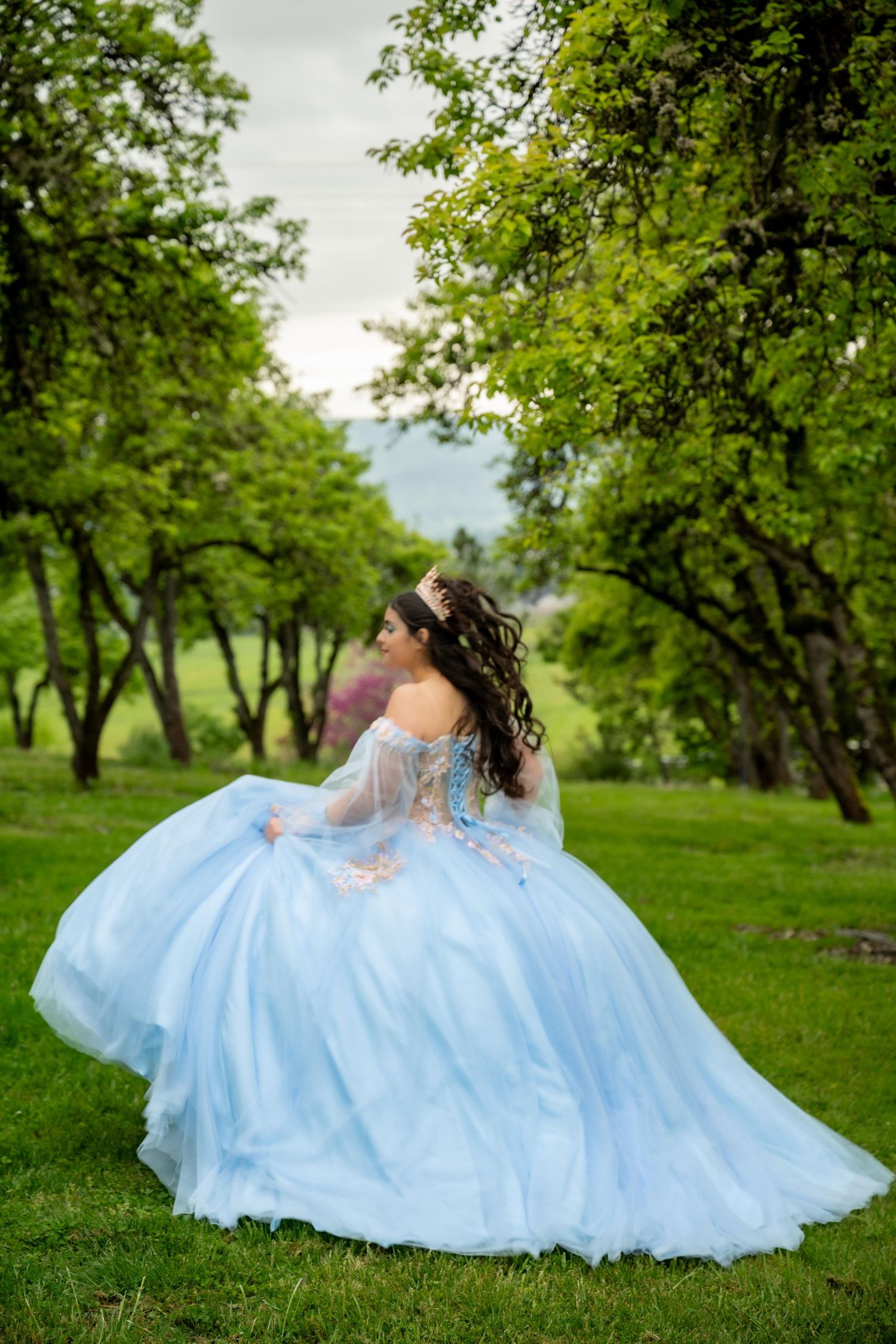 Flowing light blue ball gown with delicate details captured in an orchard setting.