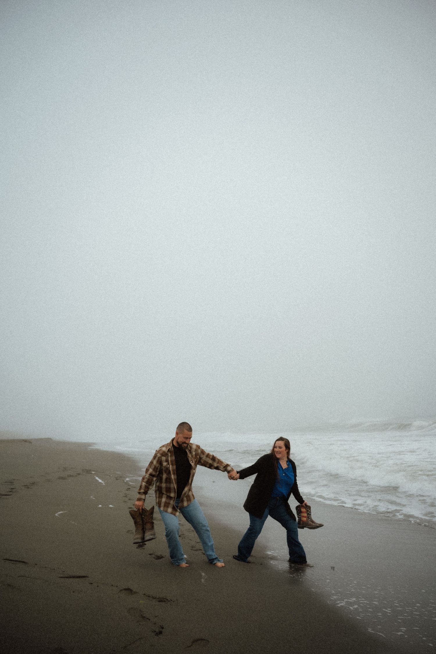 A couple plays and laughs together at the edge of the ocean waves.
