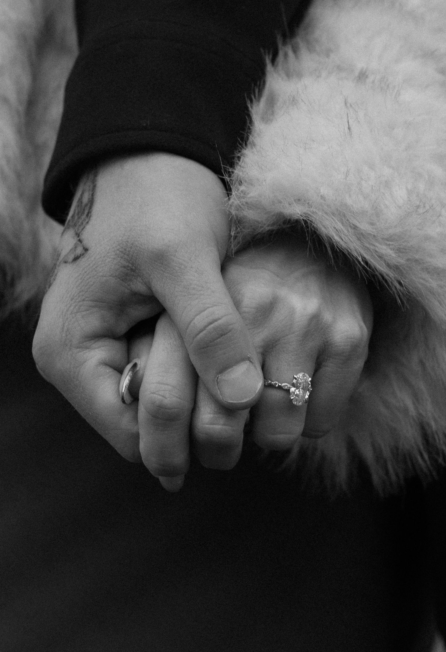 Close-up of clasped hands showing engagement ring against white fur coat background.