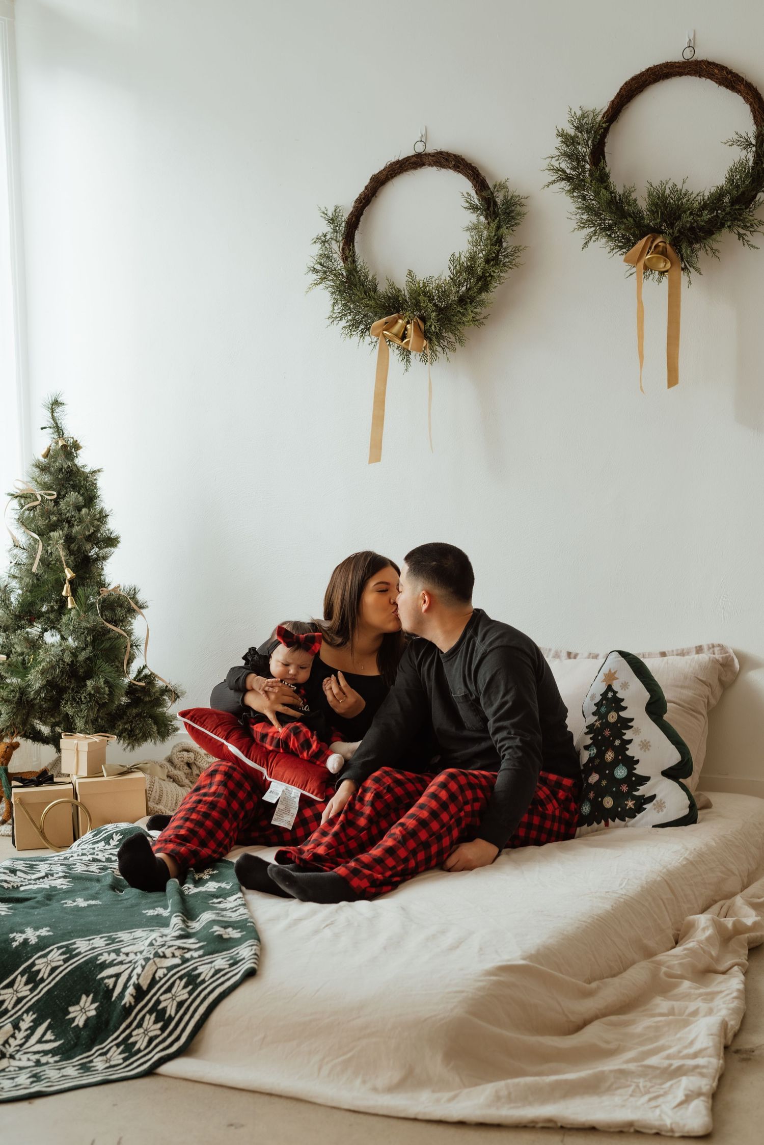 Couple in matching buffalo plaid pajamas sharing intimate moments on a couch decorated for Christmas.