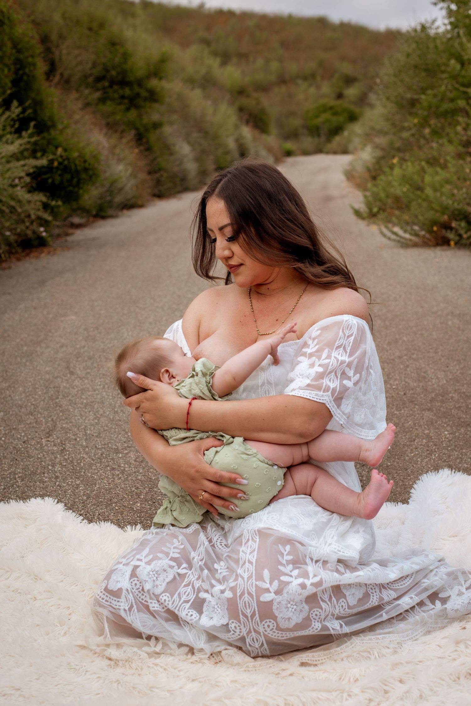 A tender nursing moment between mother and baby on a white blanket outdoors.