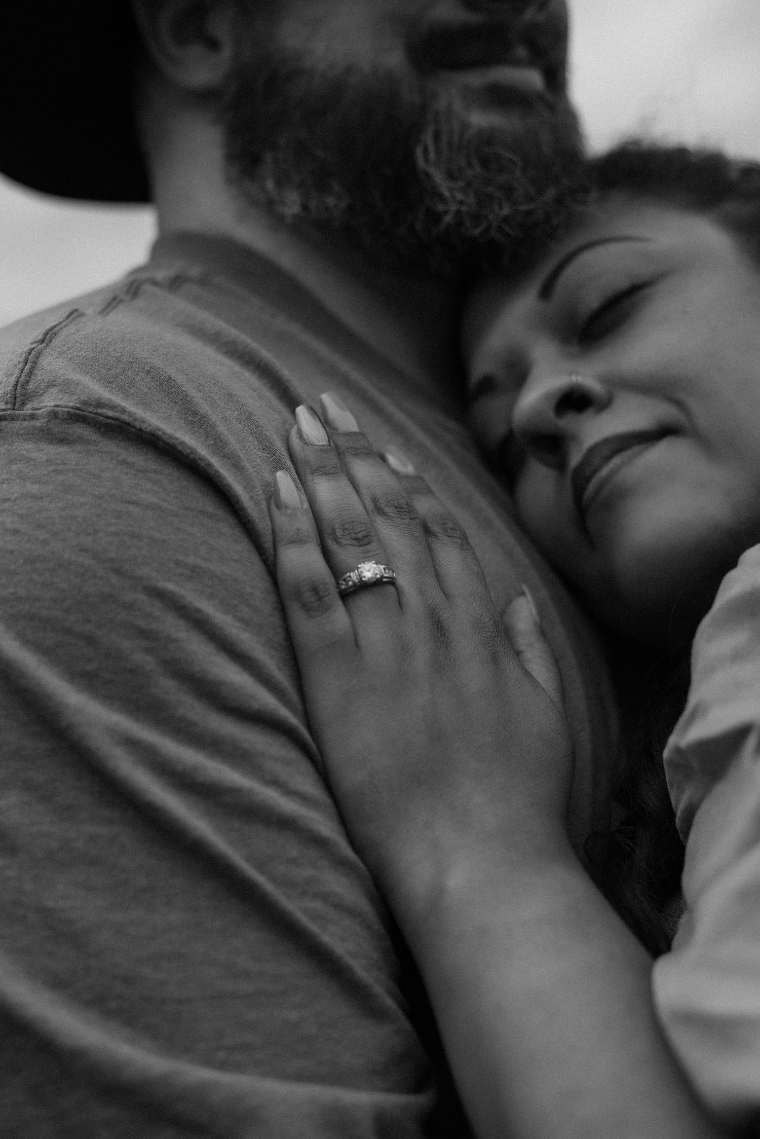 Close-up black and white photo of an intimate embrace showing hands and shoulders.