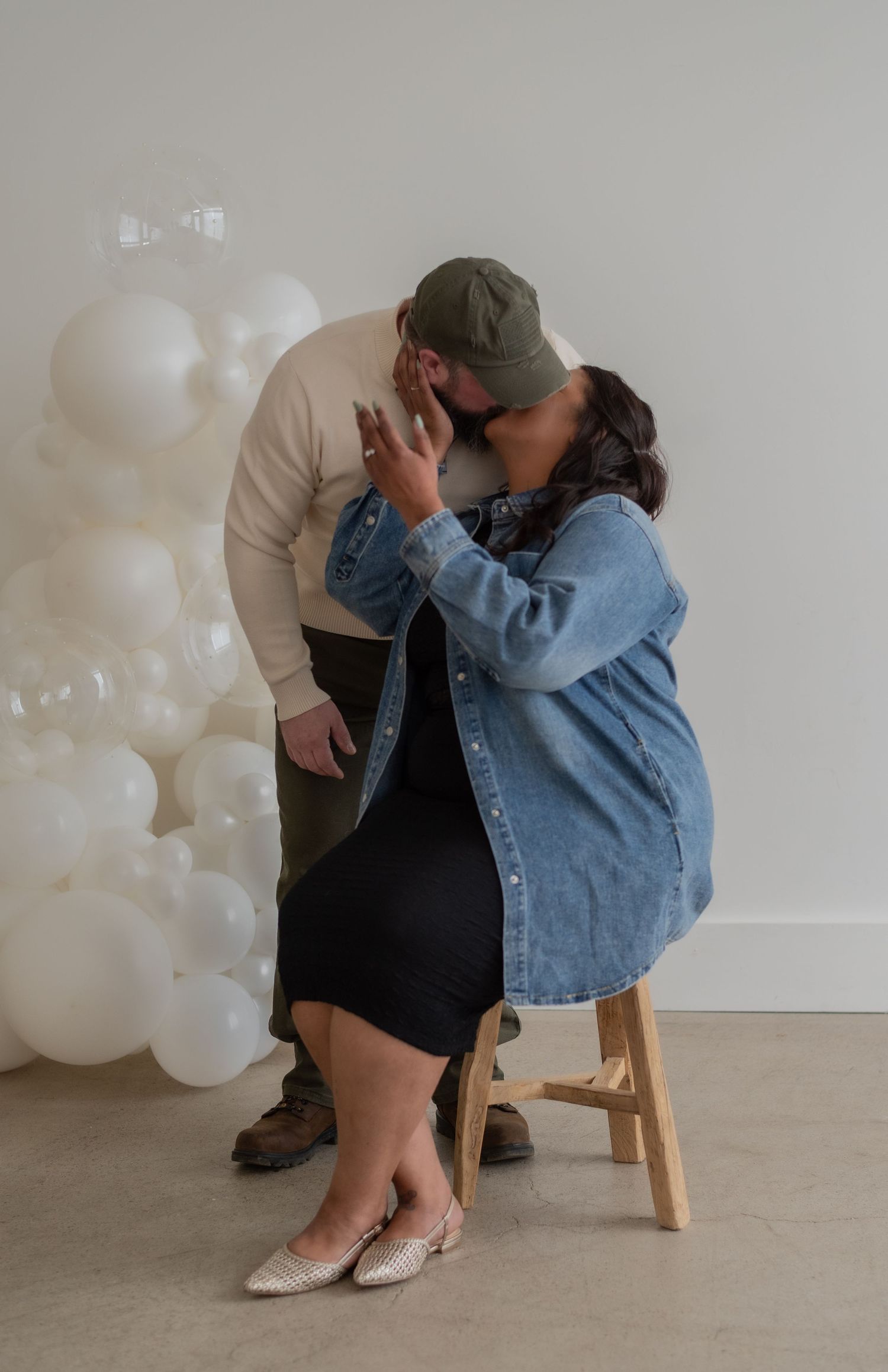 A couple shares an intimate moment in a minimalist studio setting with white balloons.