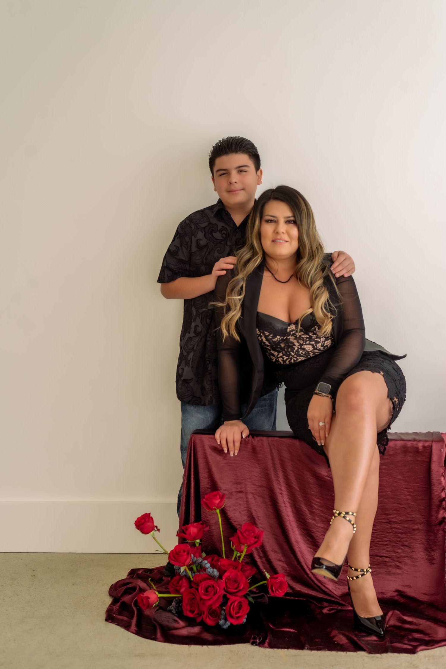 Romantic photoshoot with red roses and burgundy fabric against white backdrop.