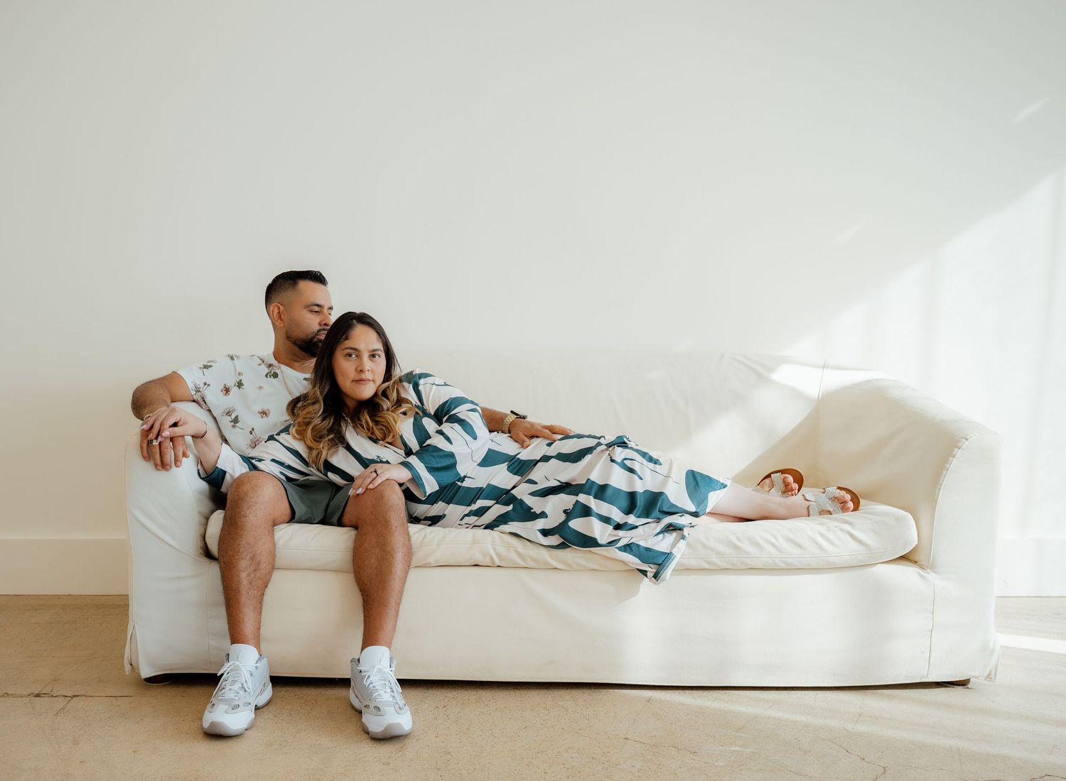 Two people sit casually together on a white couch wearing coordinated blue and white clothing.