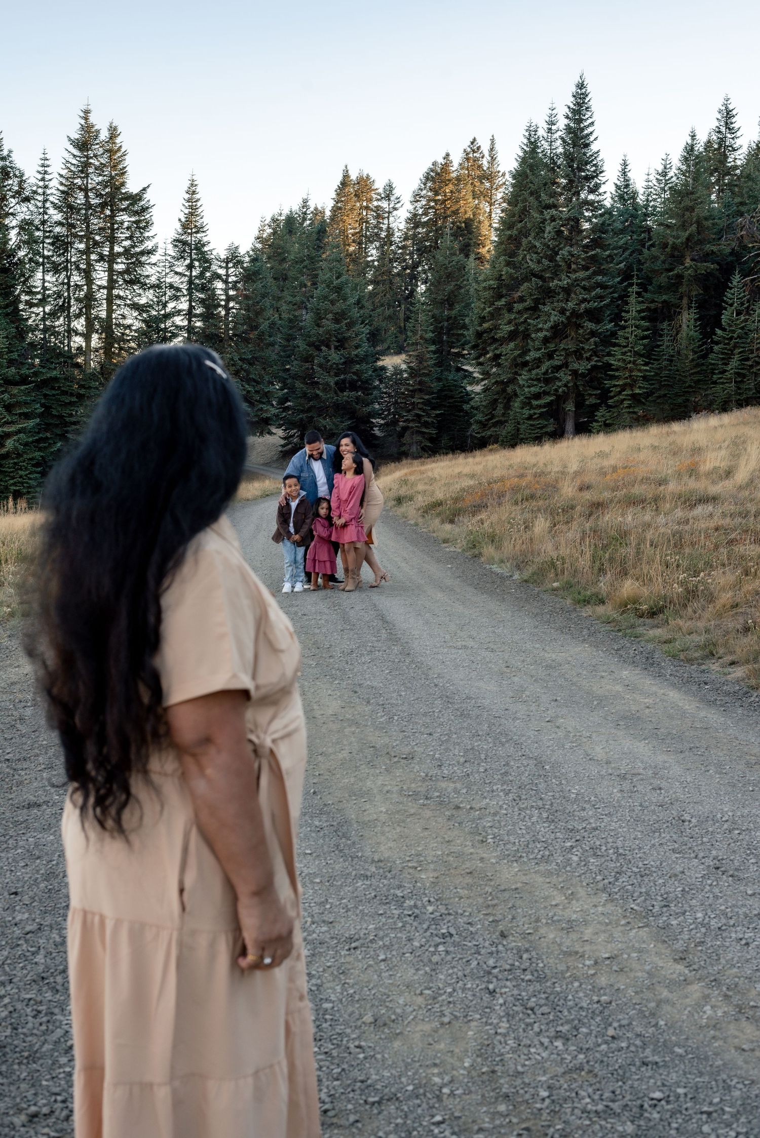 Family members walking along a gravel trail surrounded by evergreen trees.