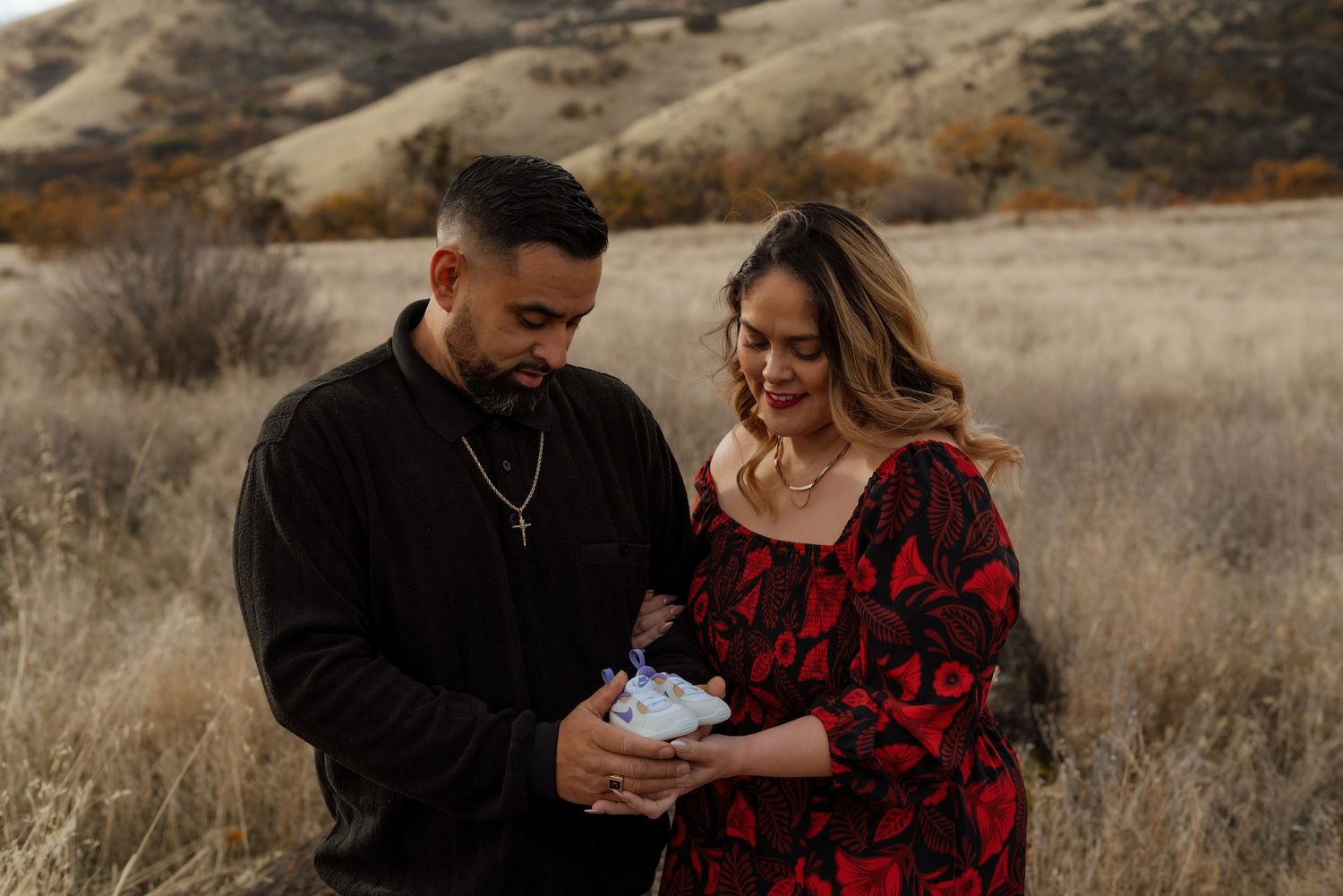 Couple shares intimate moment in autumn field with mountains in background.