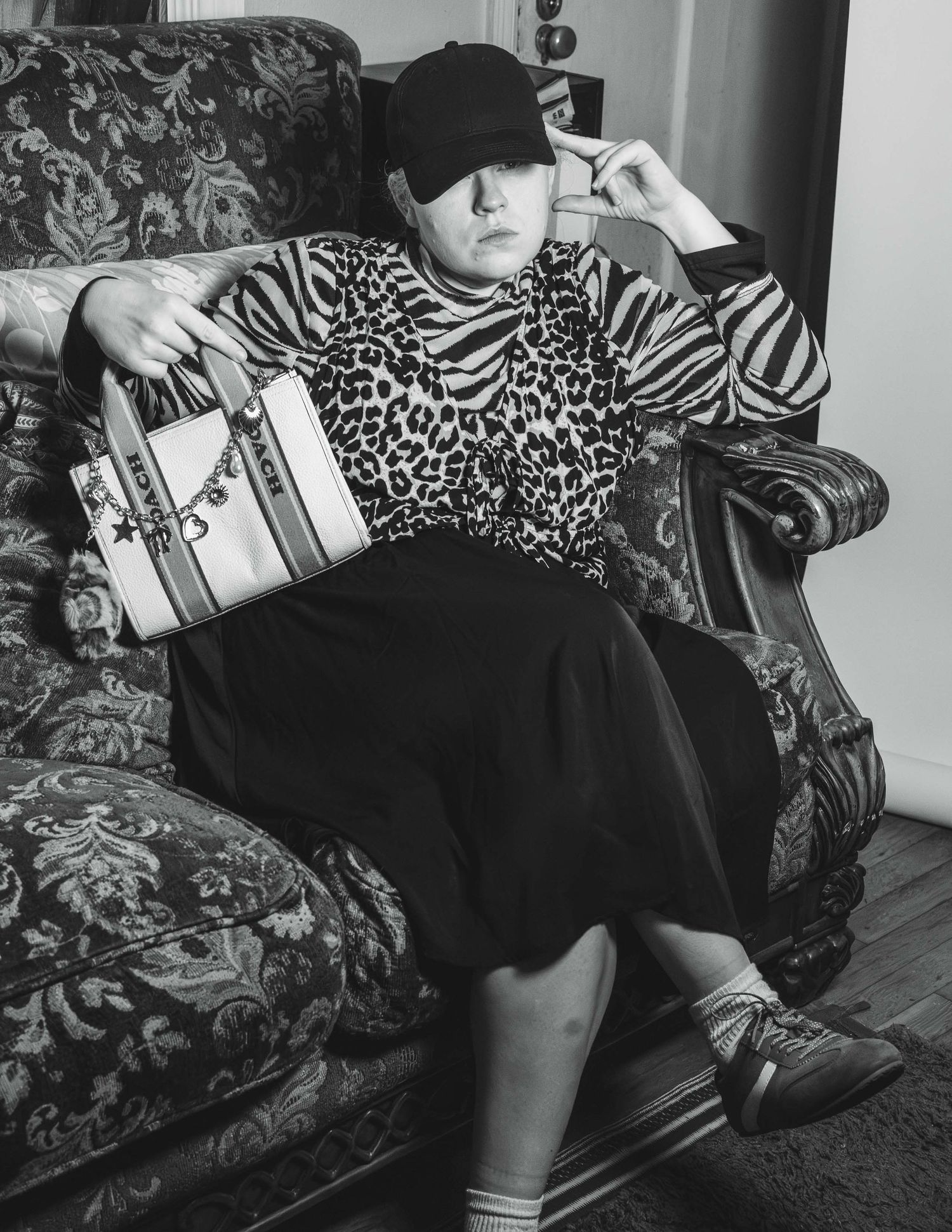 Black and white photo of person in animal print top holding handbag in armchair.