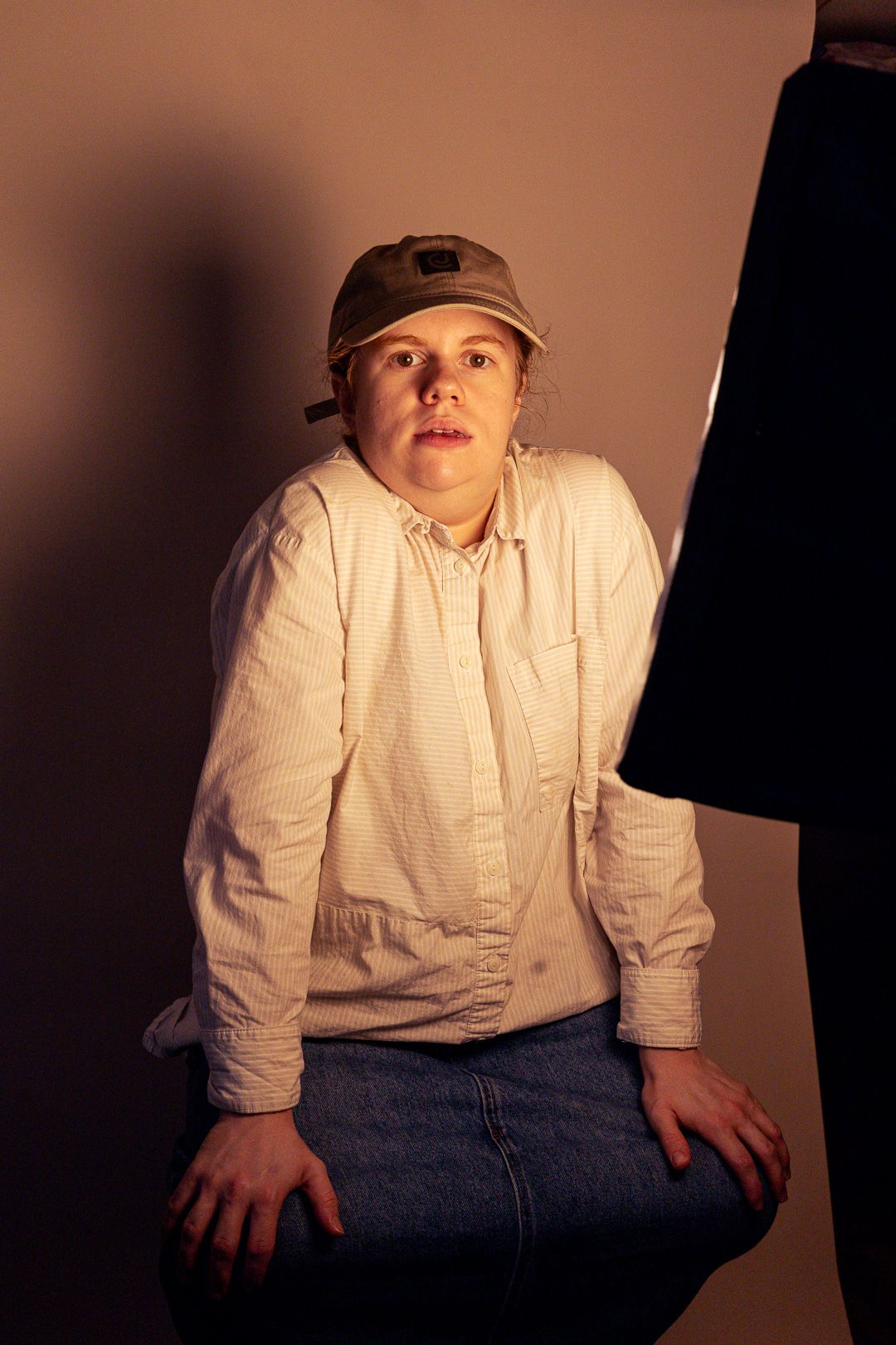 Young person in white shirt and cap crouching in dramatic studio lighting.