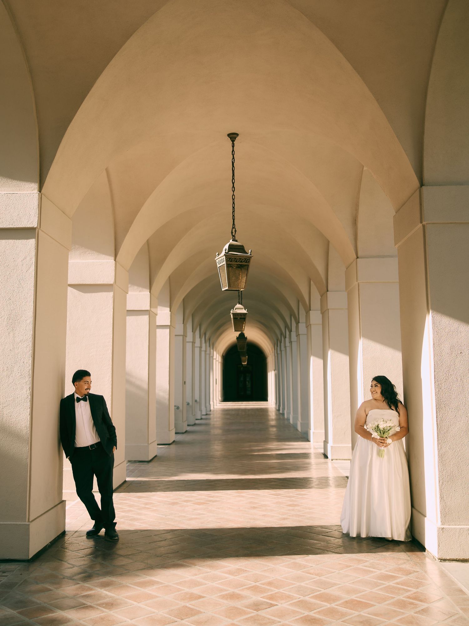 Wedding couple posing in the symmetrical arched walkways of Pasadena City Hall. Inquire for bookings.