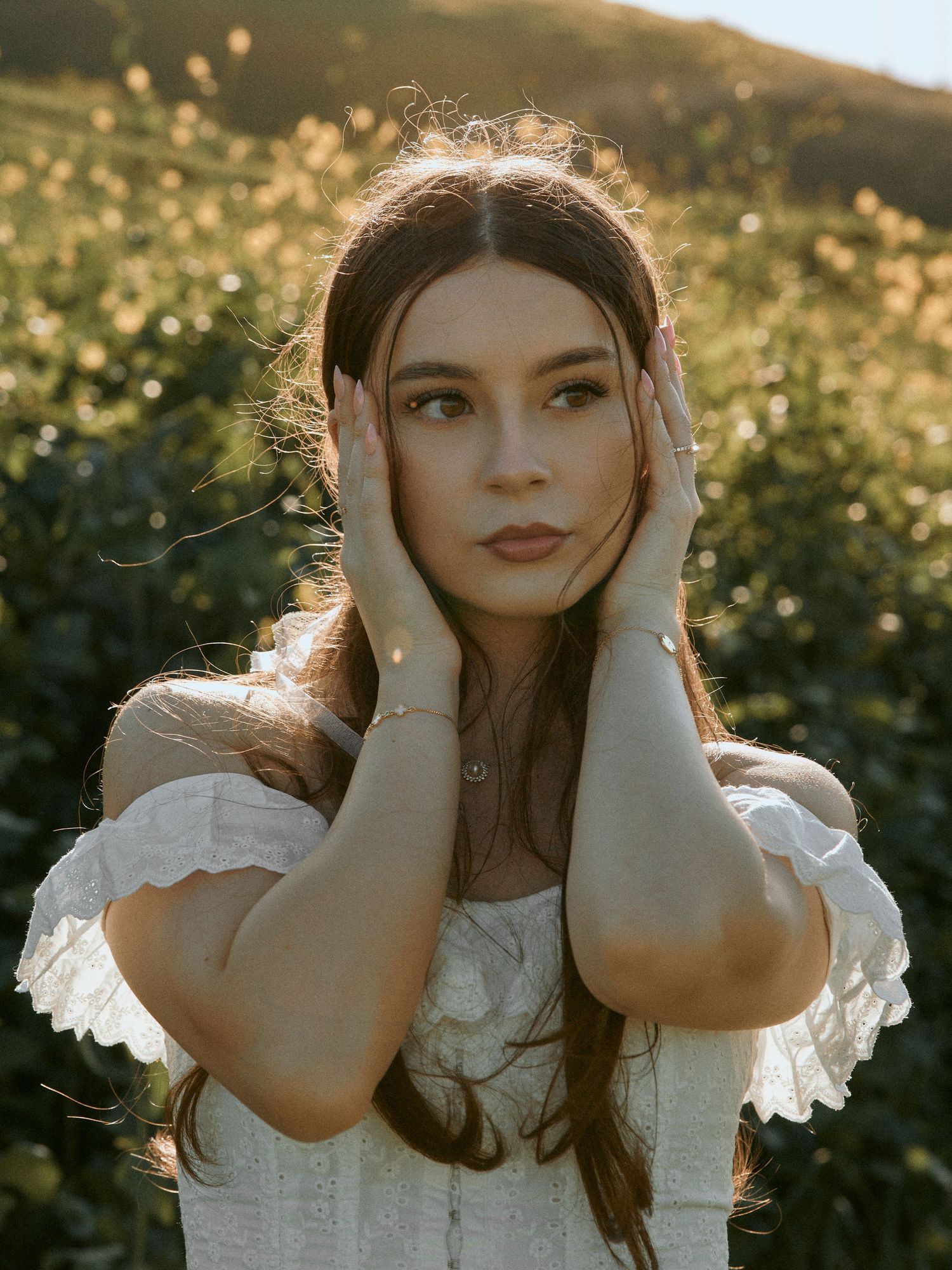 Dreamy golden hour portrait of a woman in a white off-the-shoulder dress posing in a grassy field.