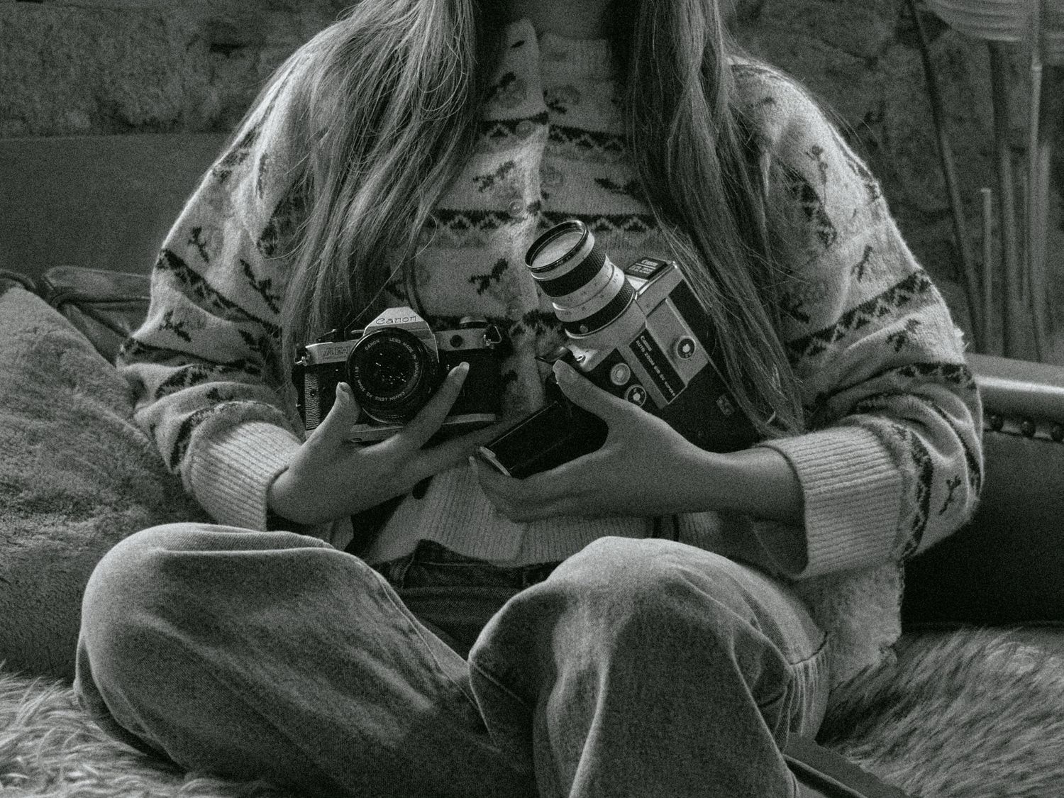 Black and white portrait of photographer sitting cross-legged holding a professional camera.