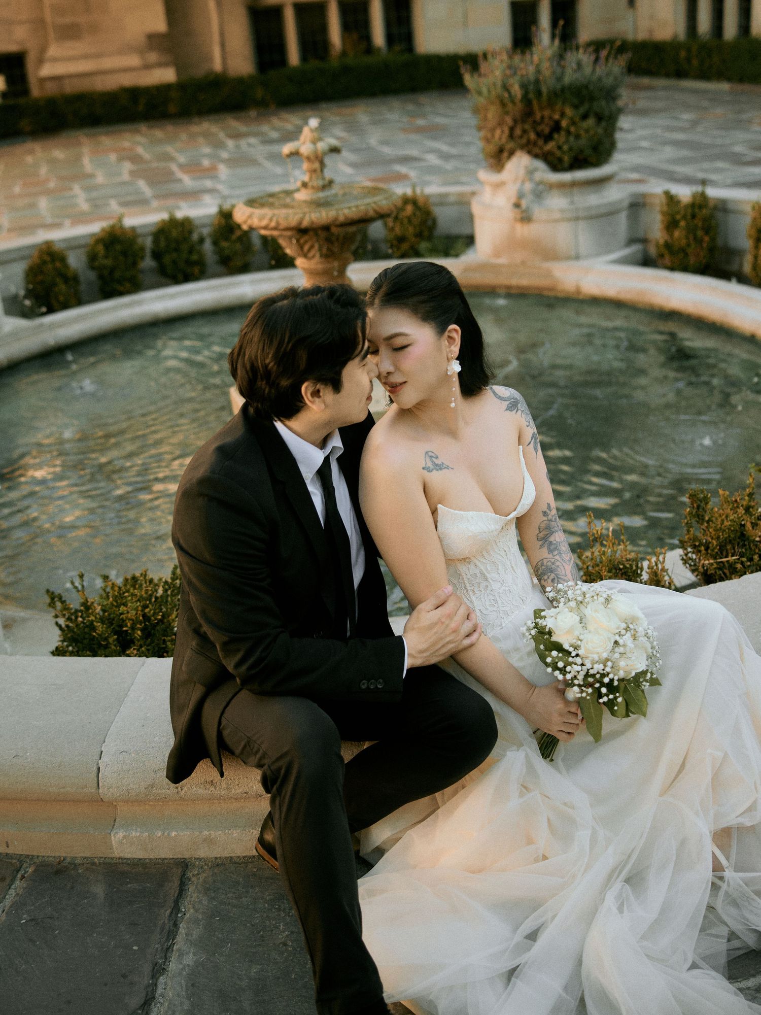 Bride and groom sharing an intimate moment seated by an outdoor stone fountain.
