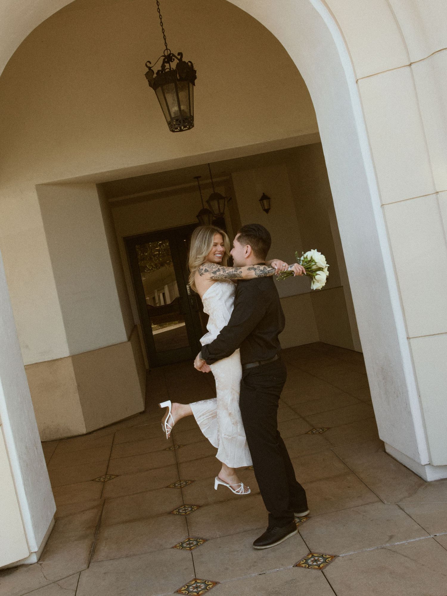 Groom holding bride under Spanish archway during Laguna Hills Civic Center elopement. Inquire for bookings.