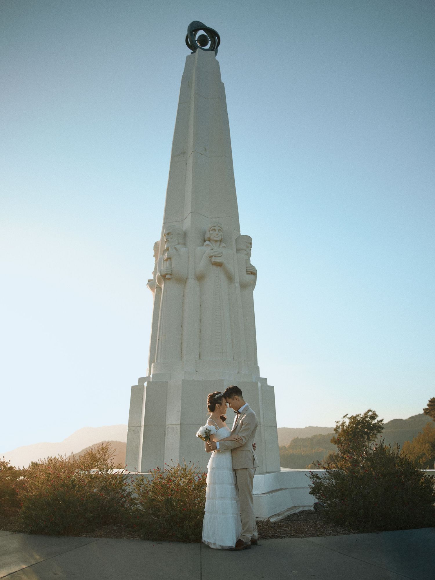 Bride and groom posing near the Astronomers Monument at Griffith Observatory. Book your LA photo session.