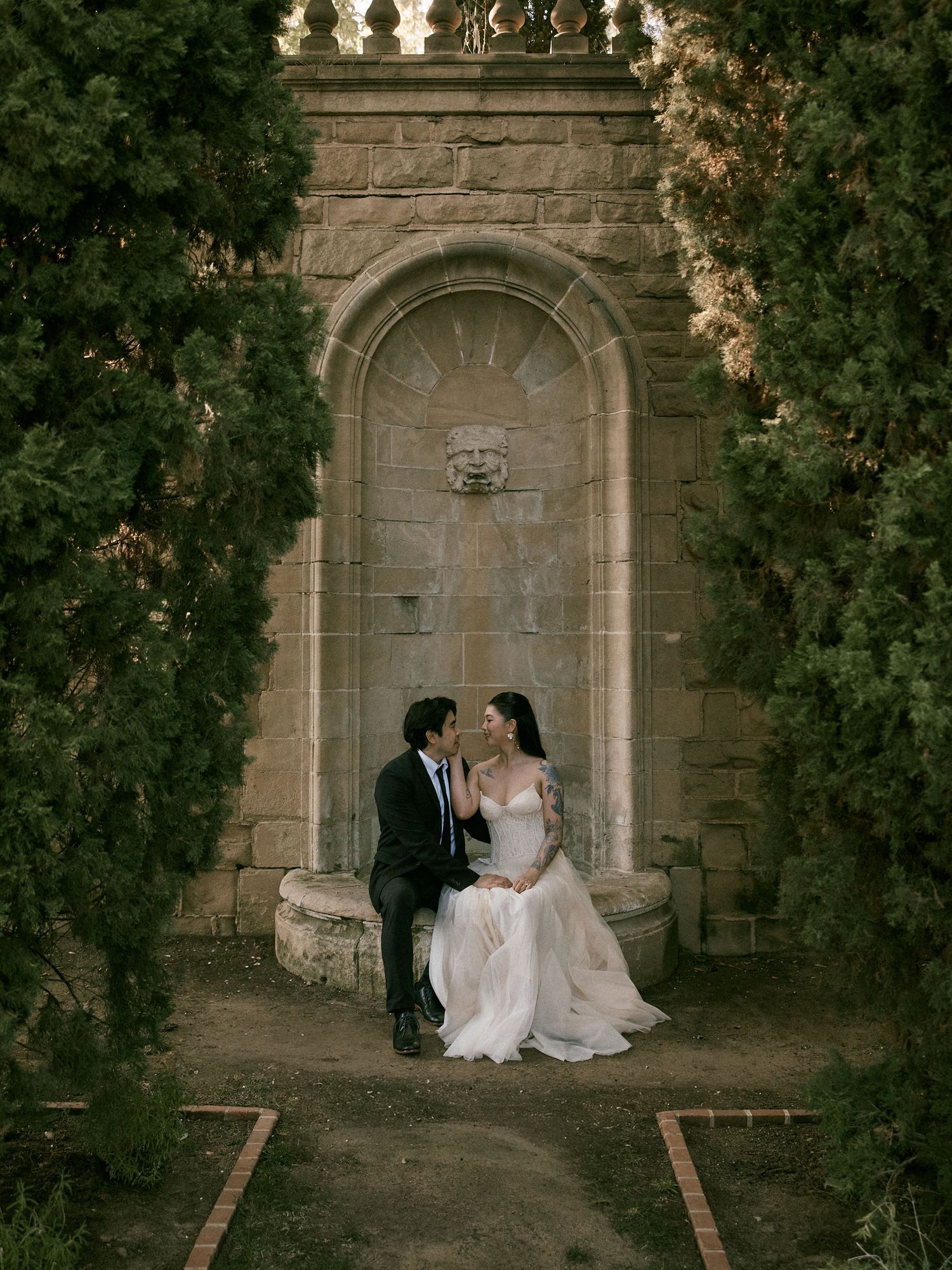 Engaged couple sitting together under a classical stone archway by Anastasiia Cuevas Photography.