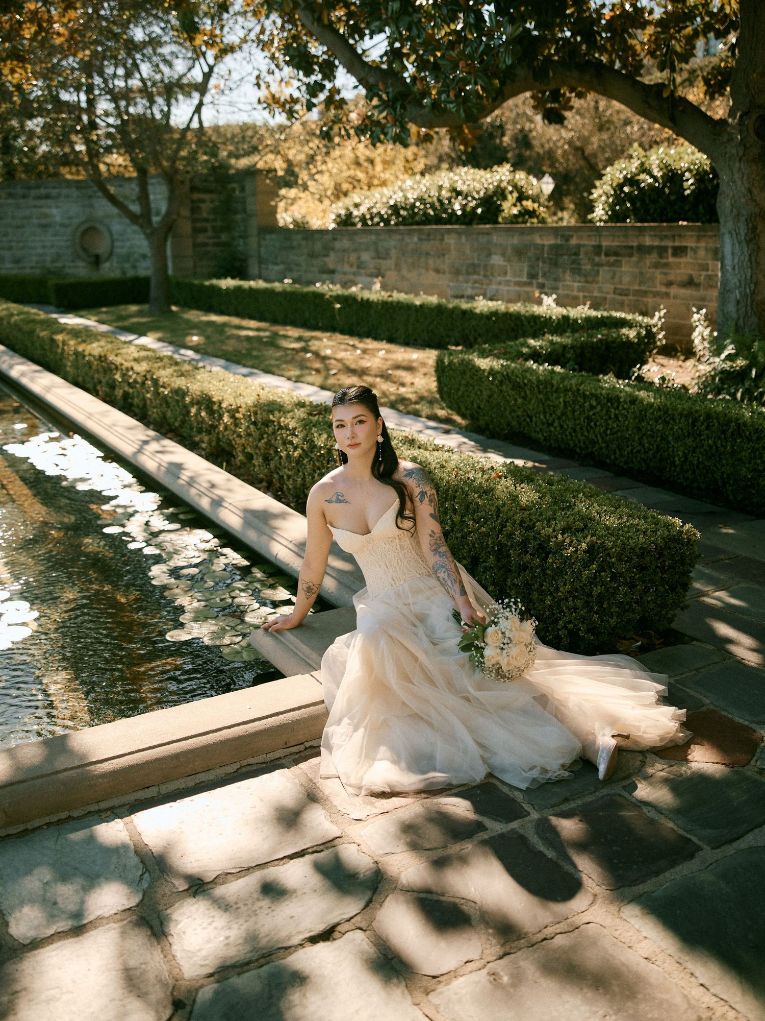 Bride sitting near a stone fountain during an engagement shoot by Anastasiia Cuevas Photography.