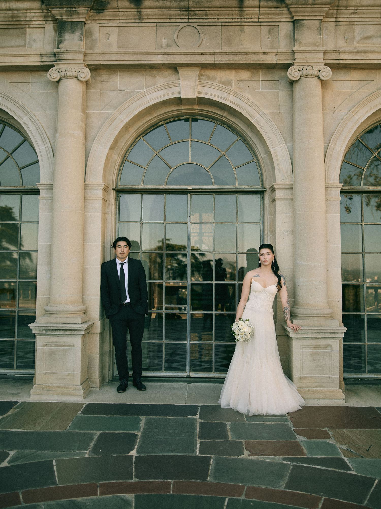 Engaged couple posing together in front of grand stone architectural archways.