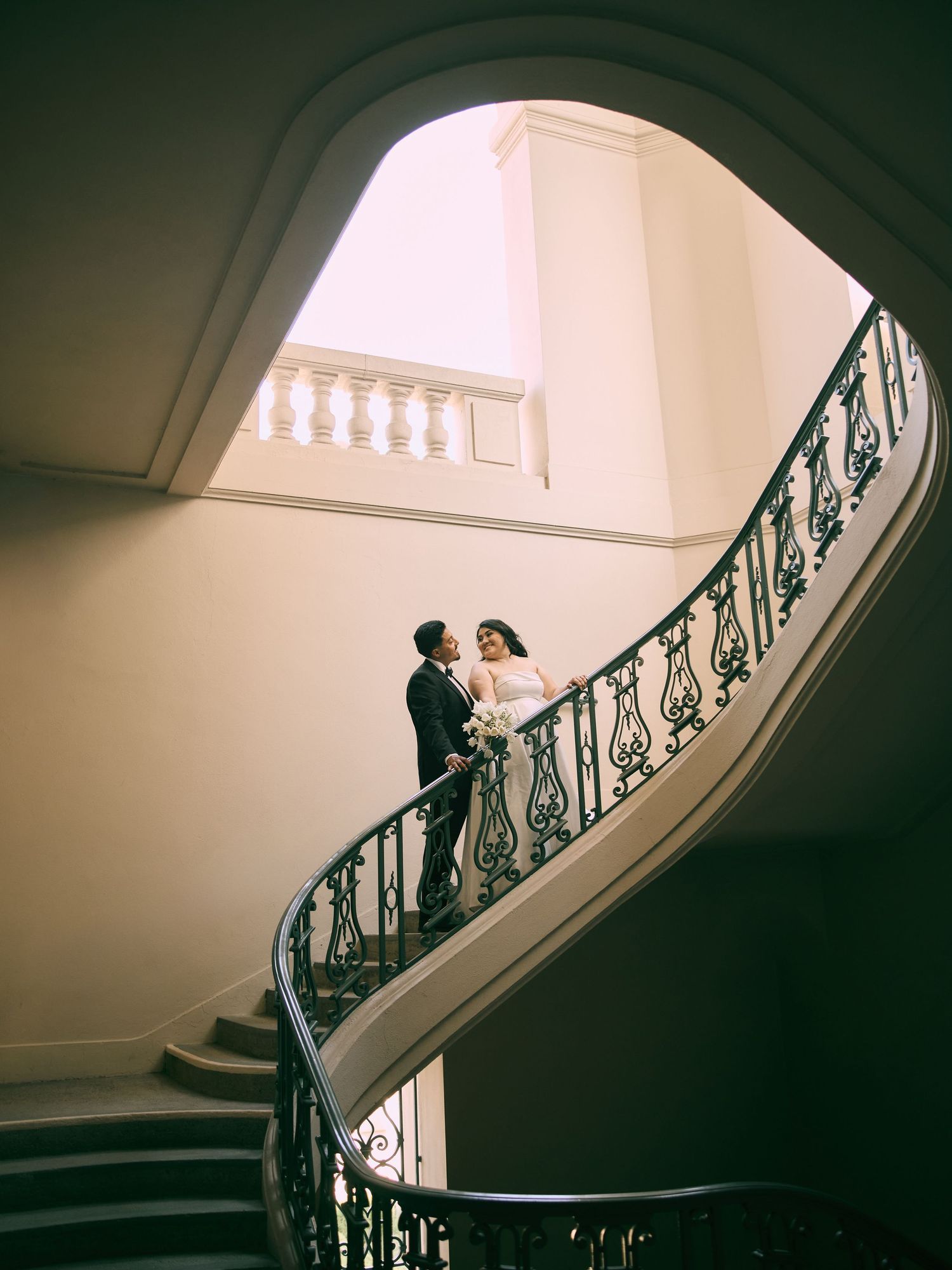 Elegant bride and groom posing on iconic curved staircase at Pasadena City Hall. Schedule your photos.
