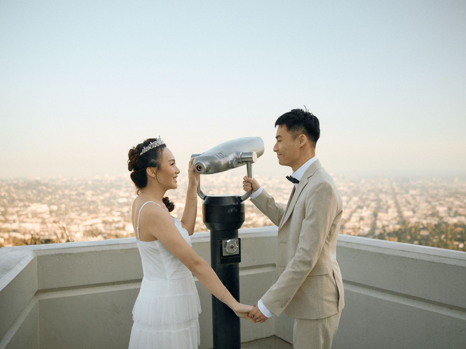 Playful engagement couple posing by the historic coin telescope on the Griffith Observatory terrace. Book your session.
