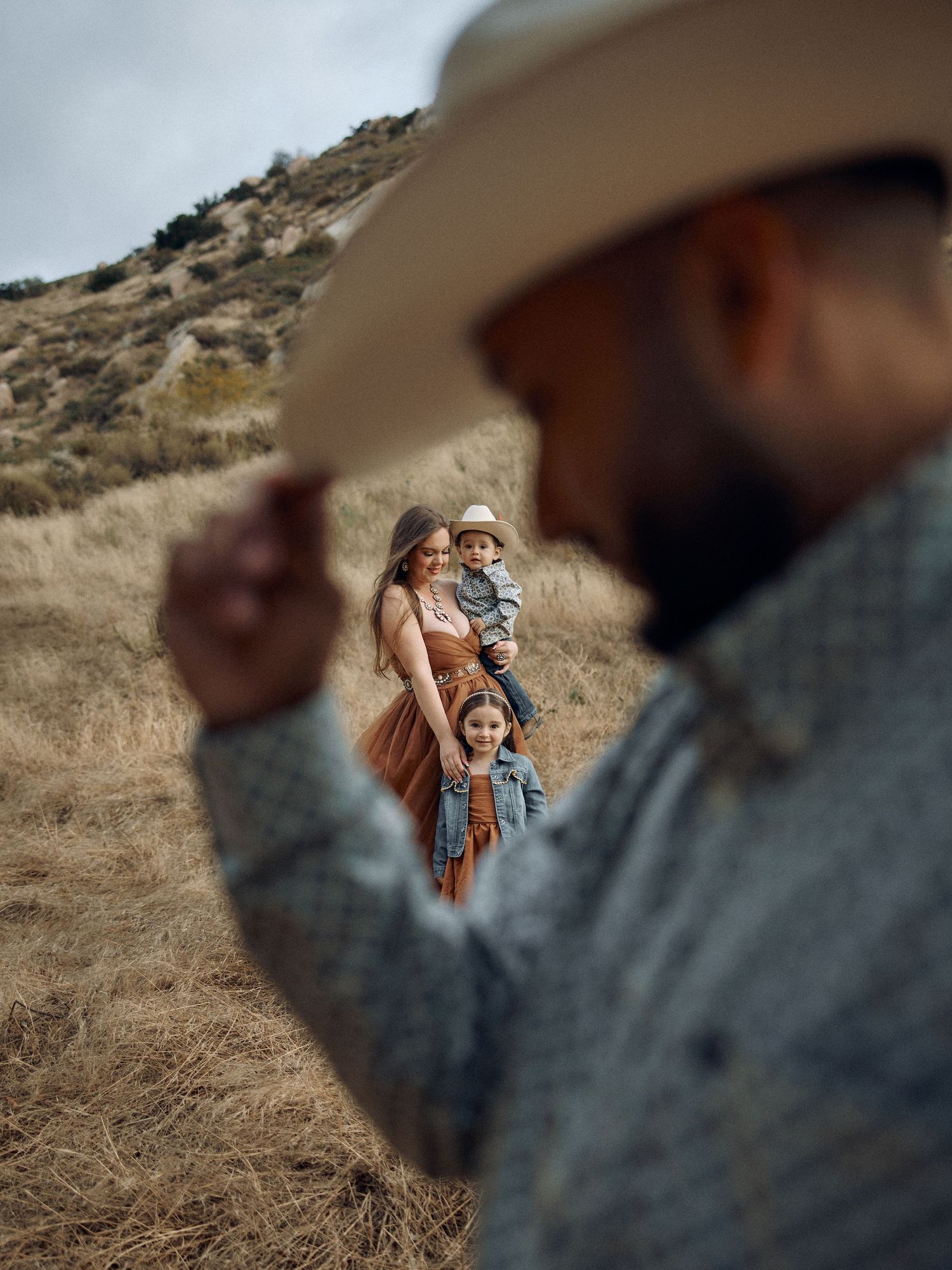 Artistic western-style family photo taken through the silhouette of a cowboy hat in a natural landscape.