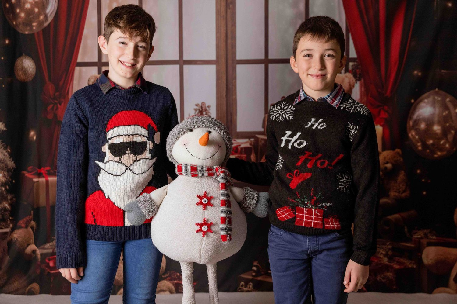 Children posing with snowman decorations in front of red curtains during Christmas photo session.