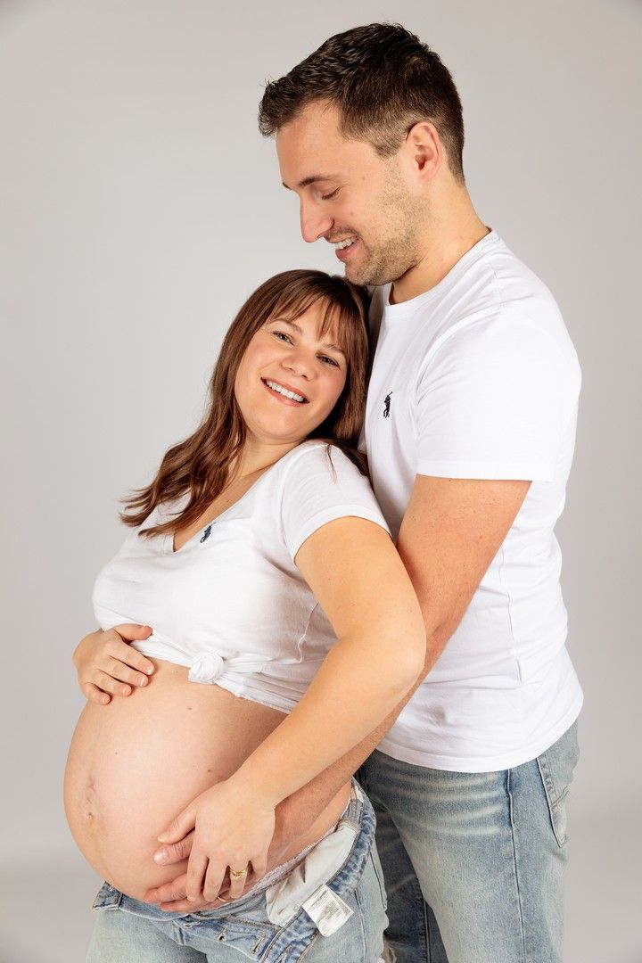 Happy expectant couple embracing, man holding pregnant womans bare belly in studio.
