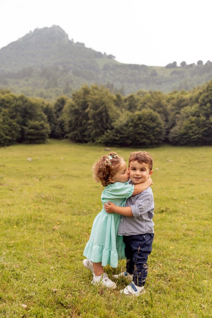 Two small children hugging in green mountain meadow.