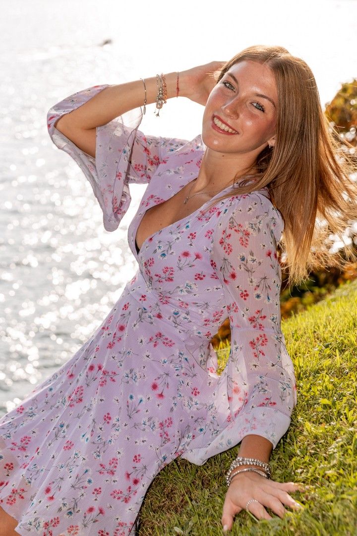 Woman in floral dress relaxing on grass by lakeside during golden hour.