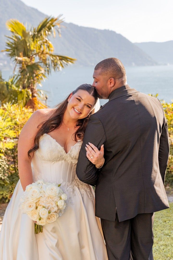 A wedding couple shares an intimate moment with white roses against a mountain backdrop.