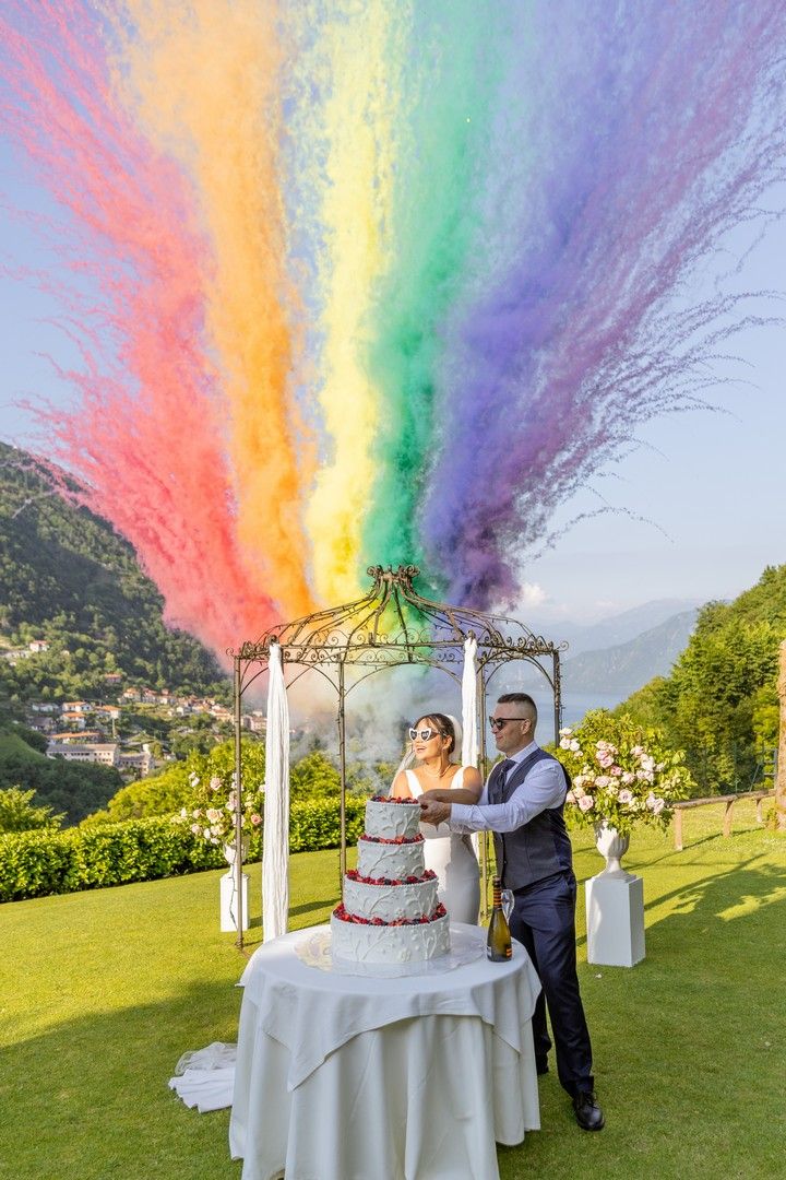 A wedding cake display outdoors with vibrant rainbow smoke effects creating a magical atmosphere.