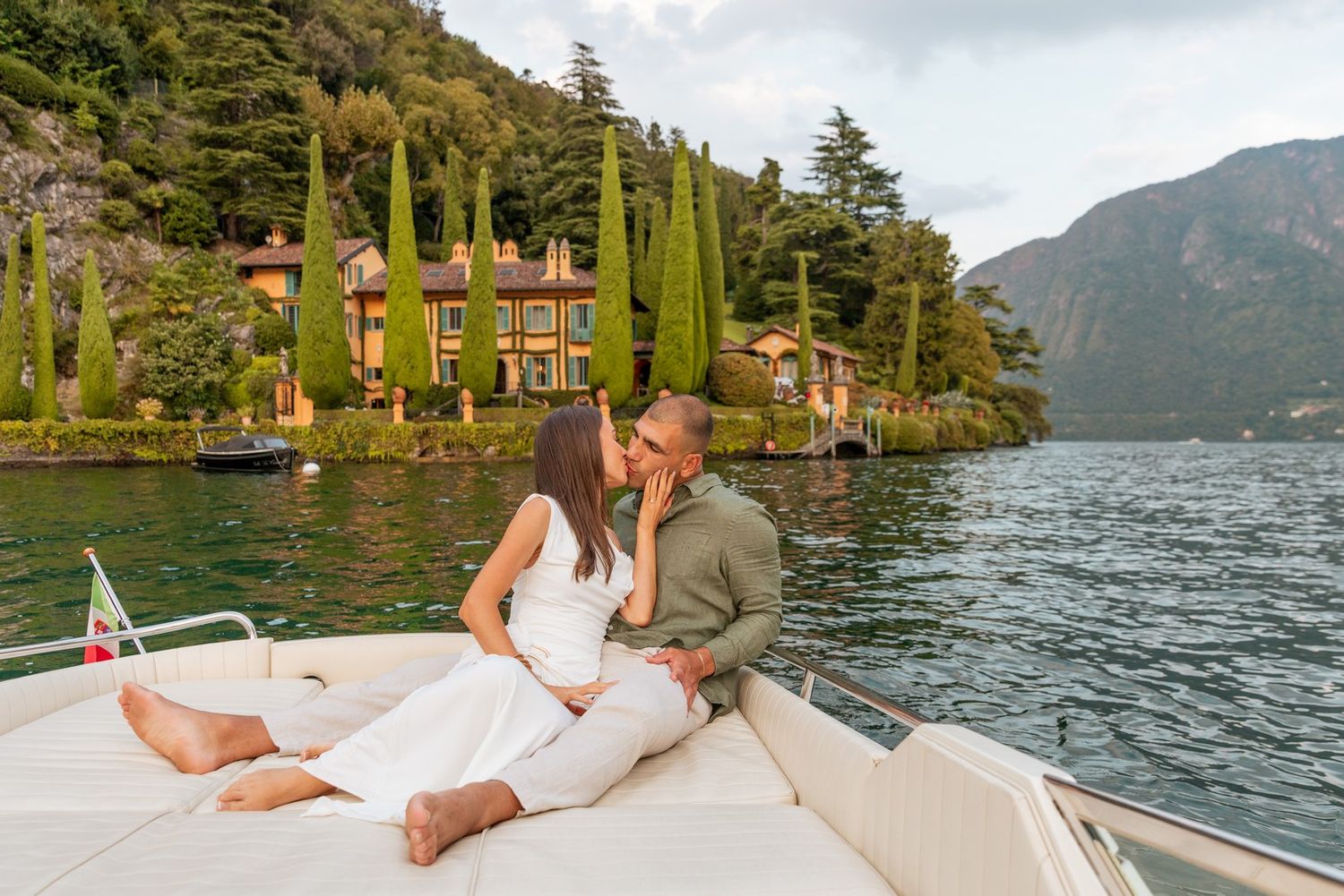 Scenic mountain lake boat ride with cypress trees and luxury villas along the shoreline.