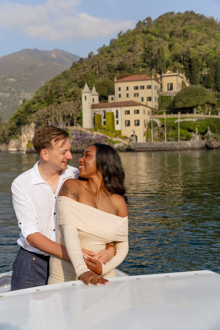 Couple embracing on a boat with Villa del Balbianello and Lake Como in the background, Italy.