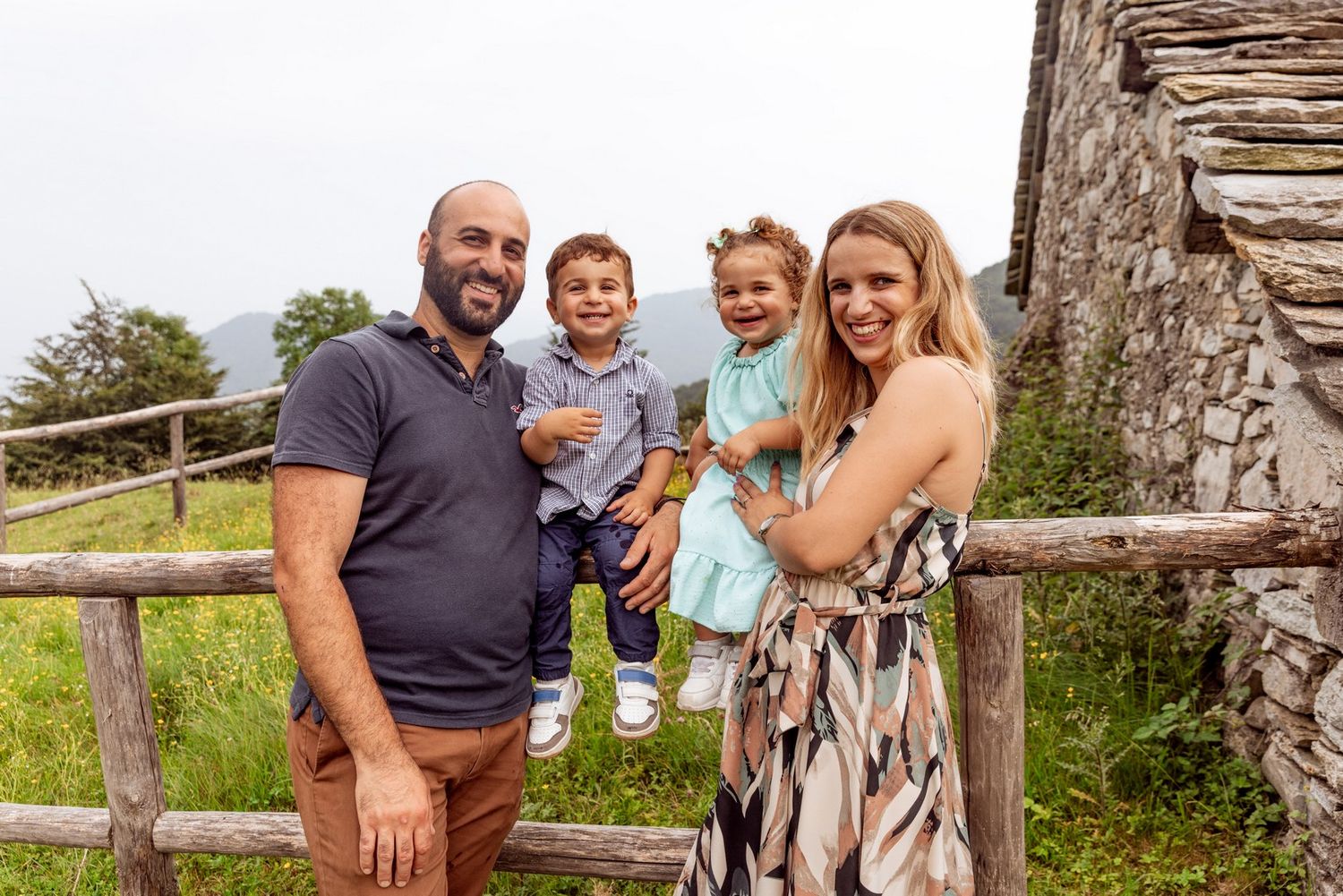 Group portrait on a stone wall with mountains and greenery in the background.